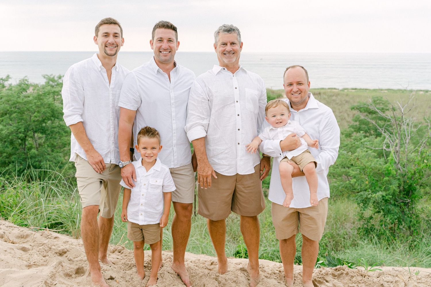 A group stands together on a sandy beach path with green coastal vegetation and ocean views in the background.
