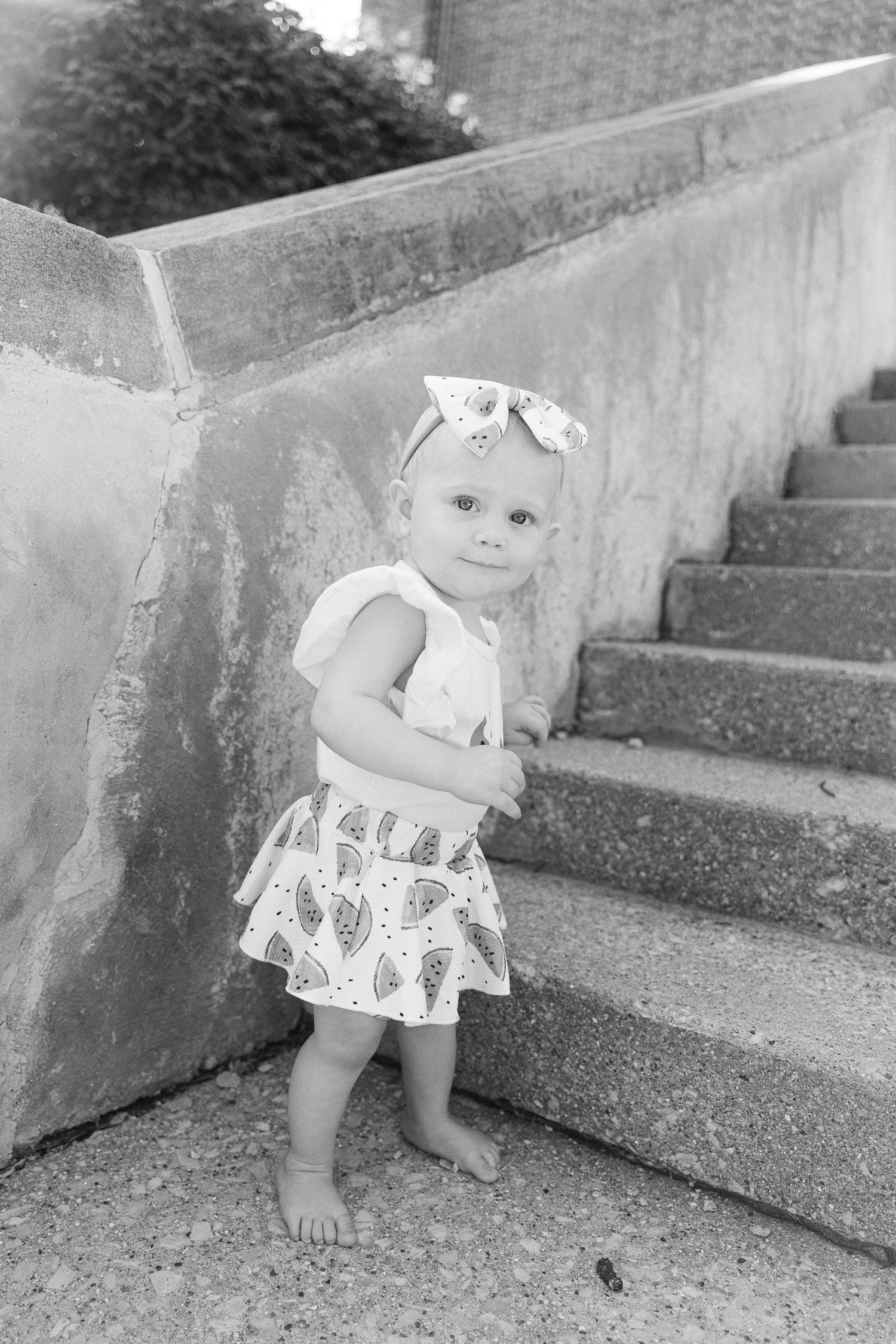 Black and white photo of small child sitting on concrete steps outdoors.