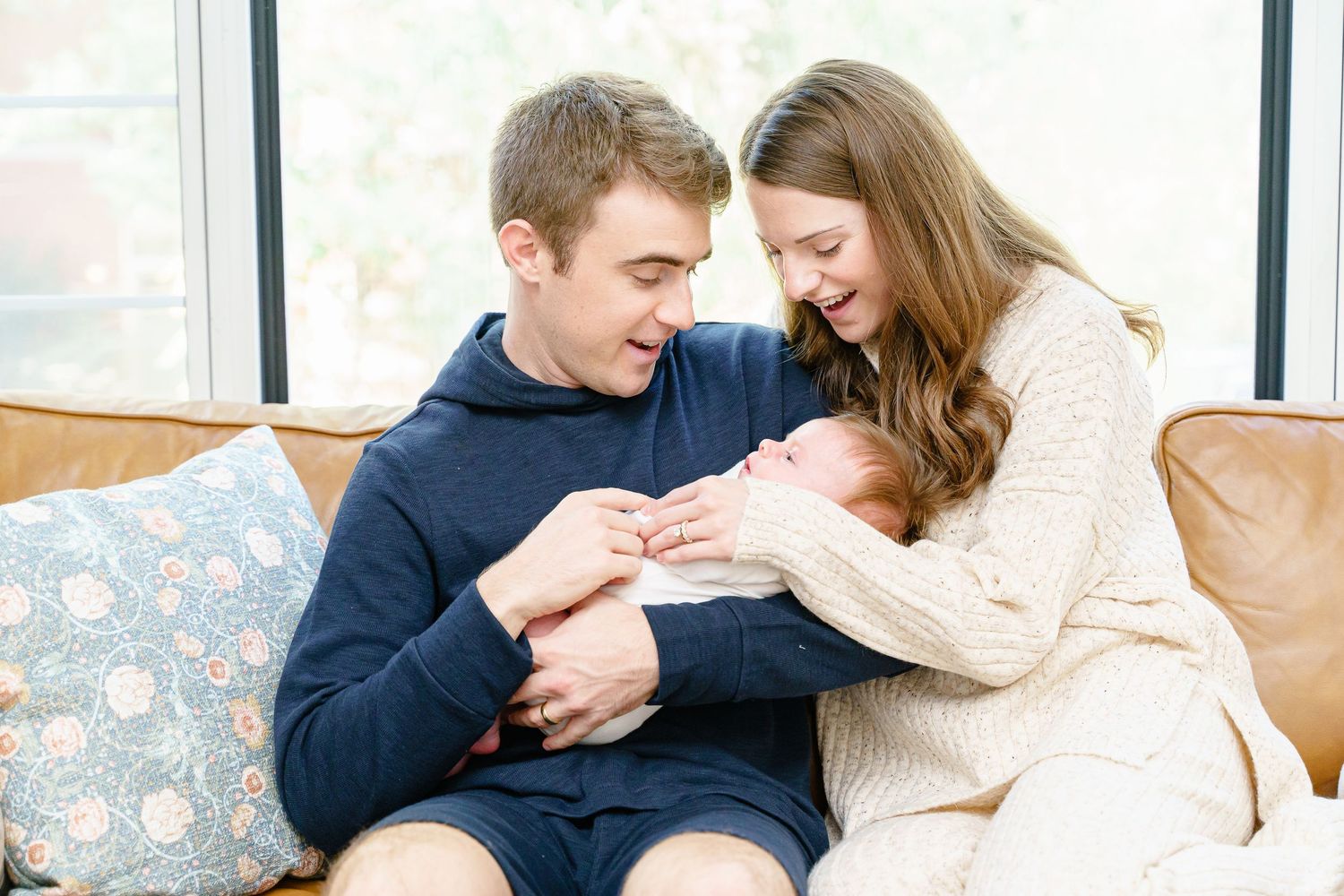 A couple sits close together on a floral couch wearing cozy sweaters while sharing a tender moment.