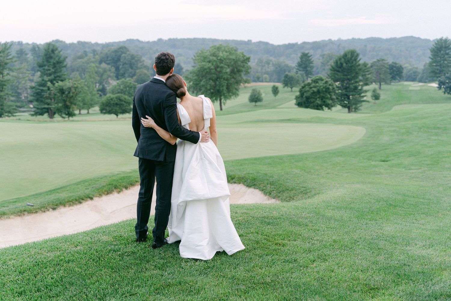 Bride and groom standing together on a lush green golf course, gazing at the scenic landscape on their wedding day in Philadelphia, PA