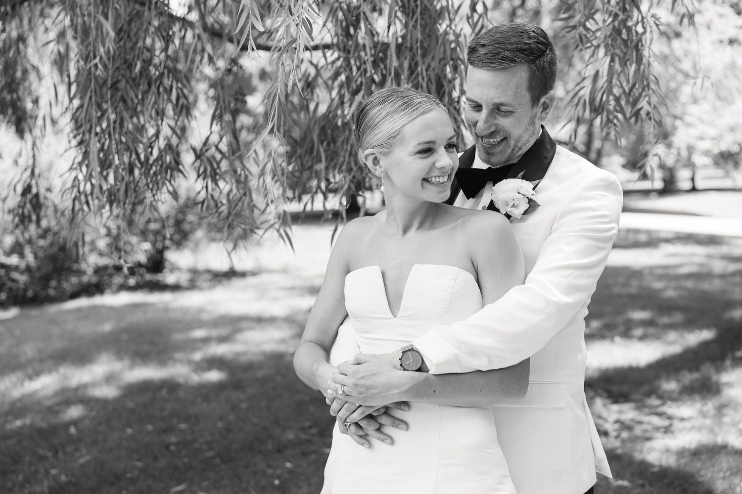 Black and white photo of a bride and groom embracing under willow tree branches, smiling joyfully on their wedding day in South Bend, IN