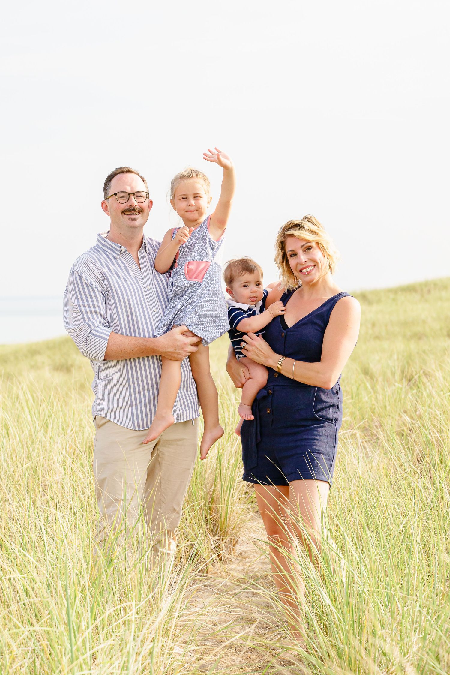 A happy family laughs and plays together in a sunlit field of tall grass on a bright summer day.