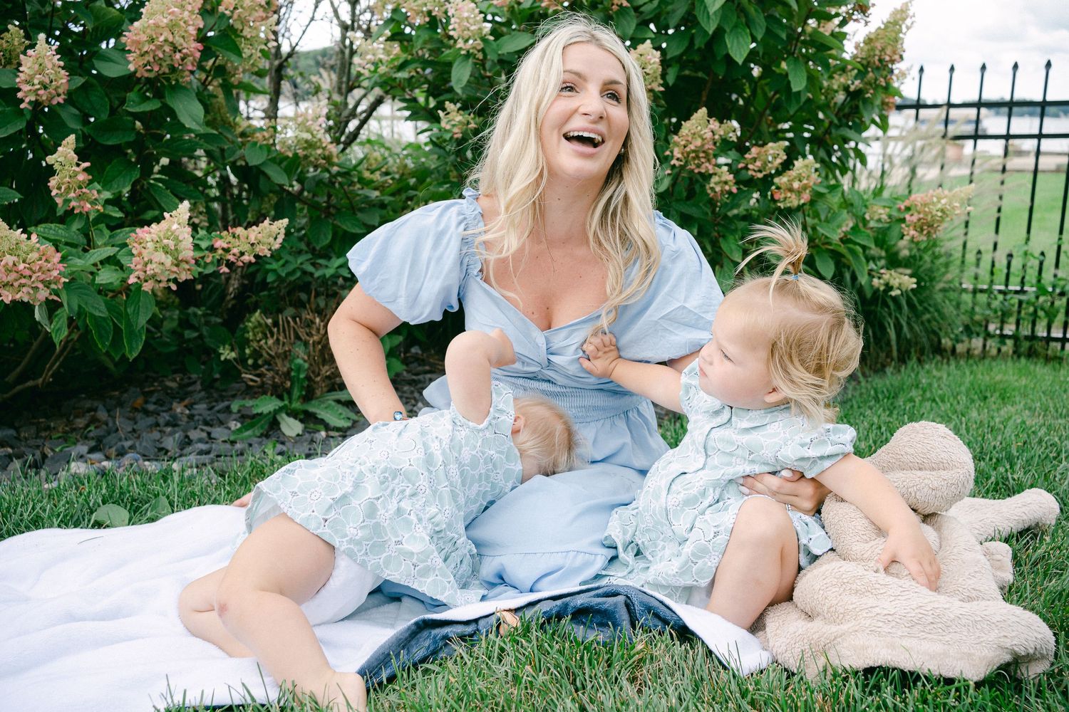 A joyful outdoor family moment captured on a white blanket beneath blooming hydrangea bushes.