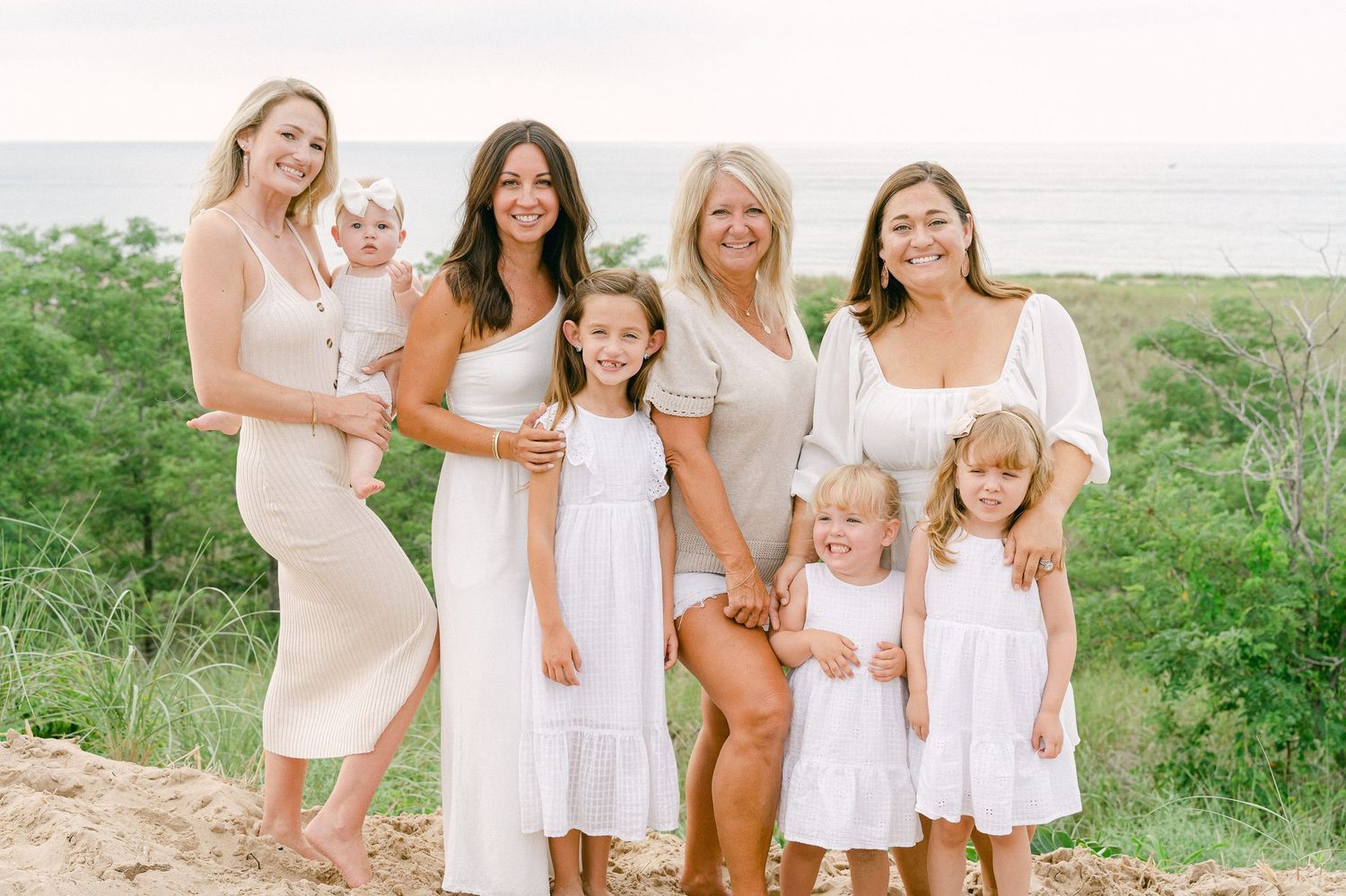 Family group wearing coordinated white outfits poses together on a beach during sunset.