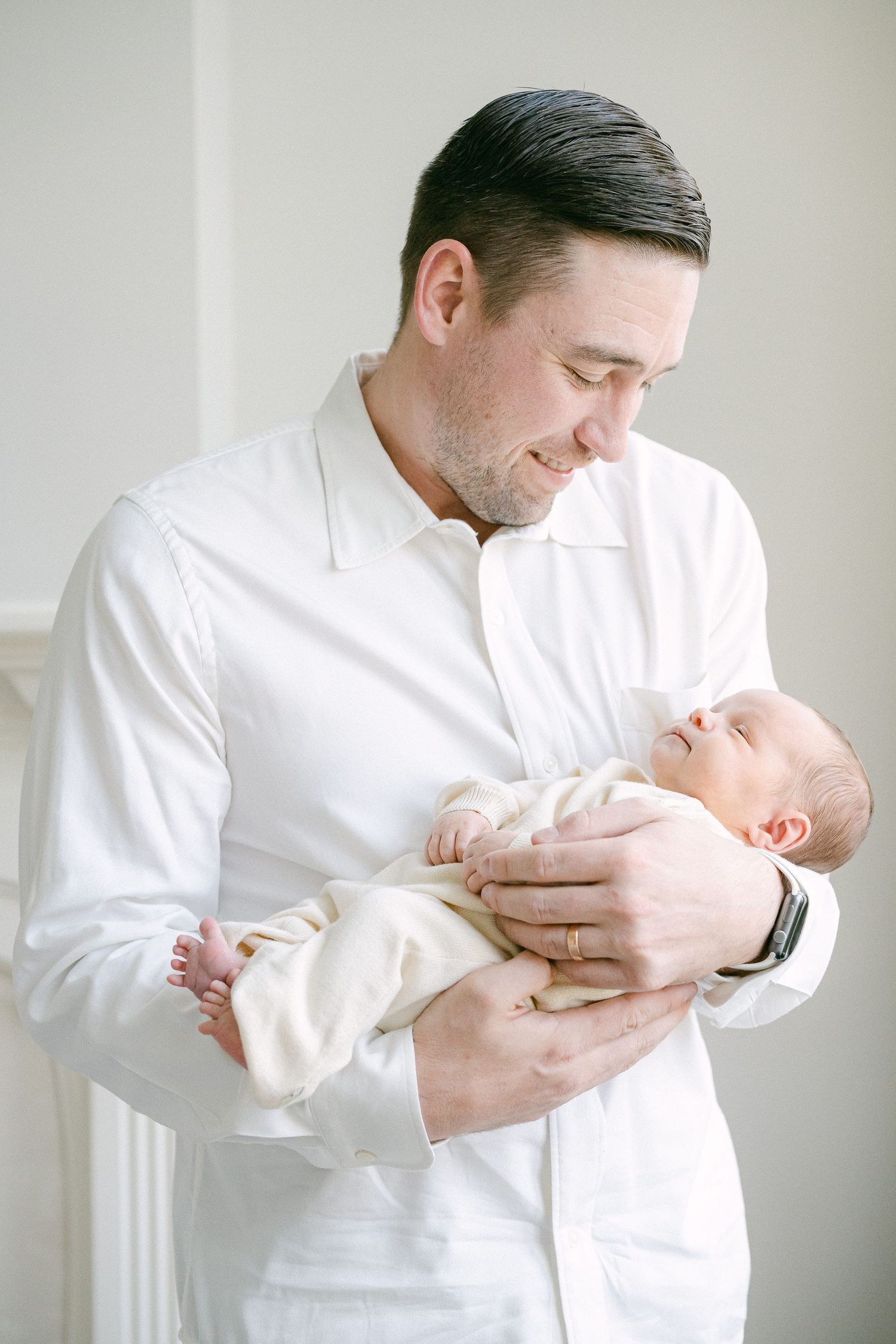 A series of tender moments showing someone in a white shirt holding and cradling a newborn baby wrapped in white fabric.