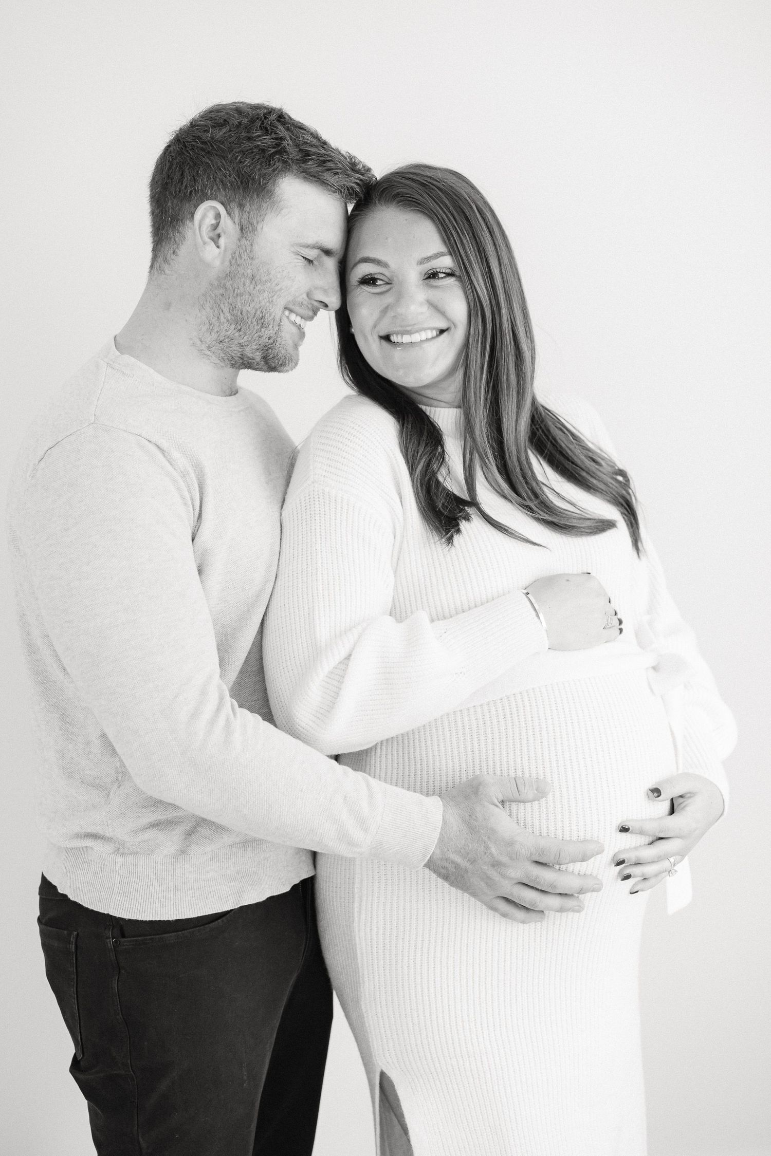 A couple in white and black clothing share intimate moments in a black and white maternity photoshoot series.