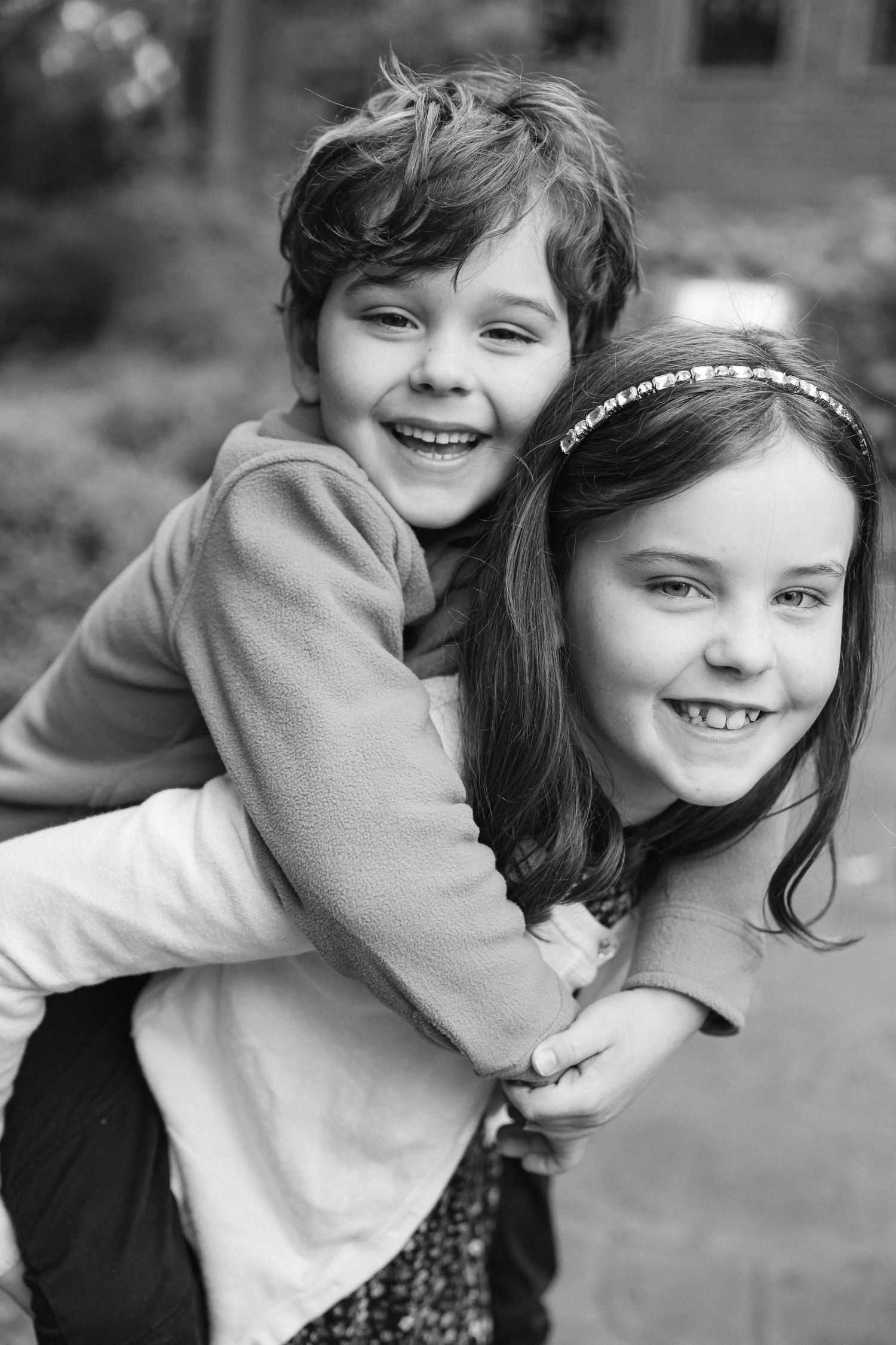 A black and white photo series showing two children hugging and laughing together in casual outdoor portraits.