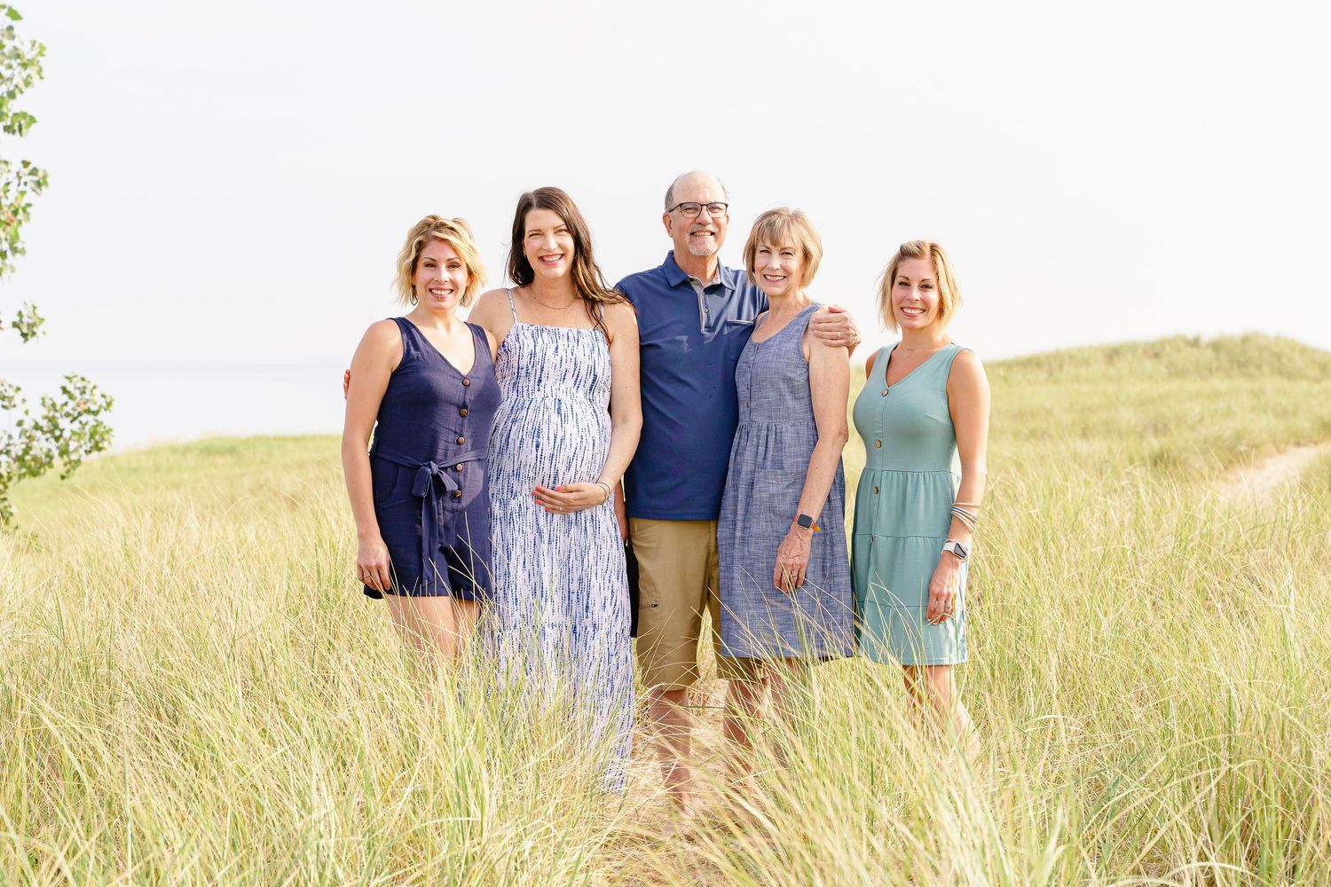 A group of people standing together in casual summer attire on a grassy hill during a sunny day.
