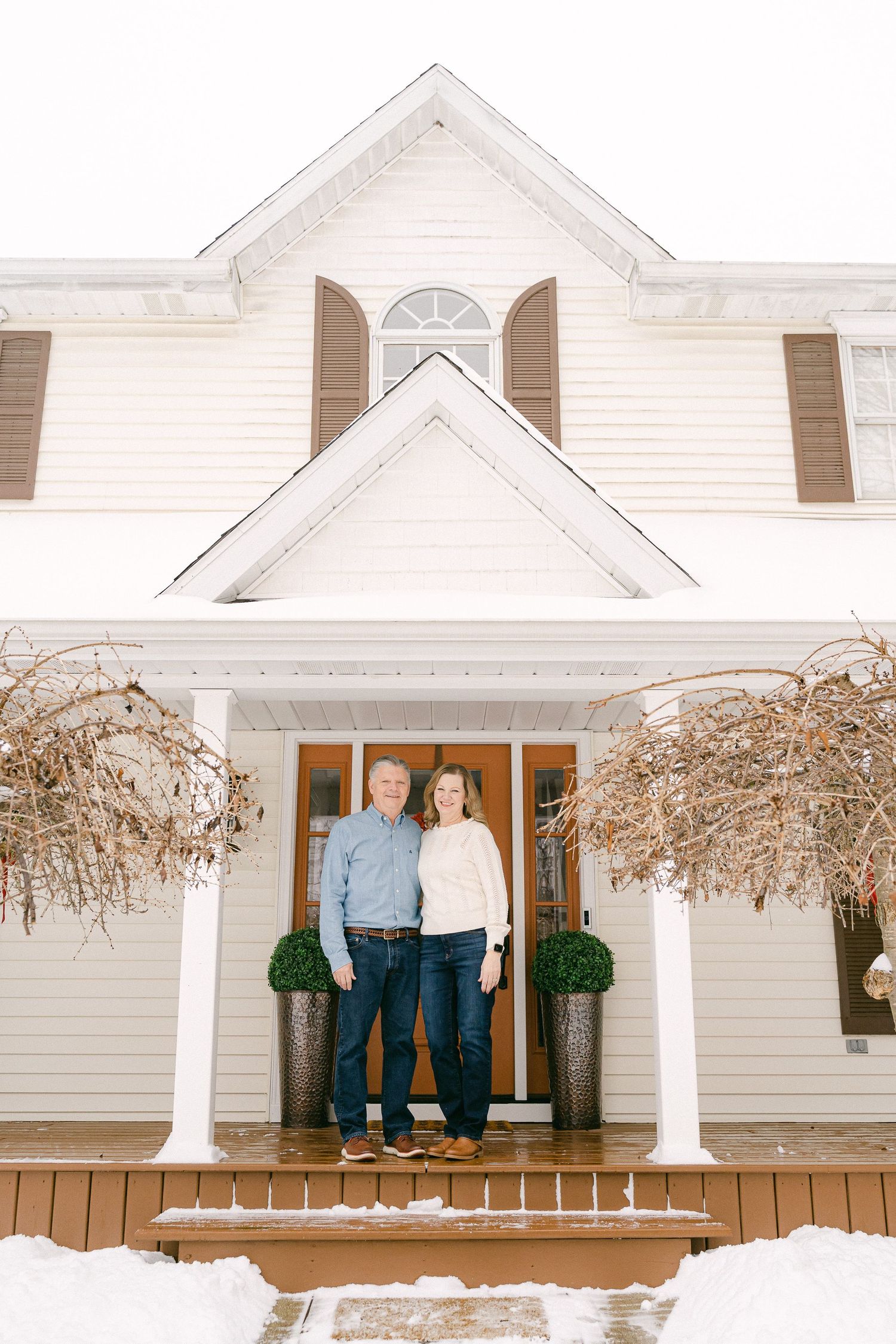 White farmhouse style home with columns and two people standing in doorway during winter.