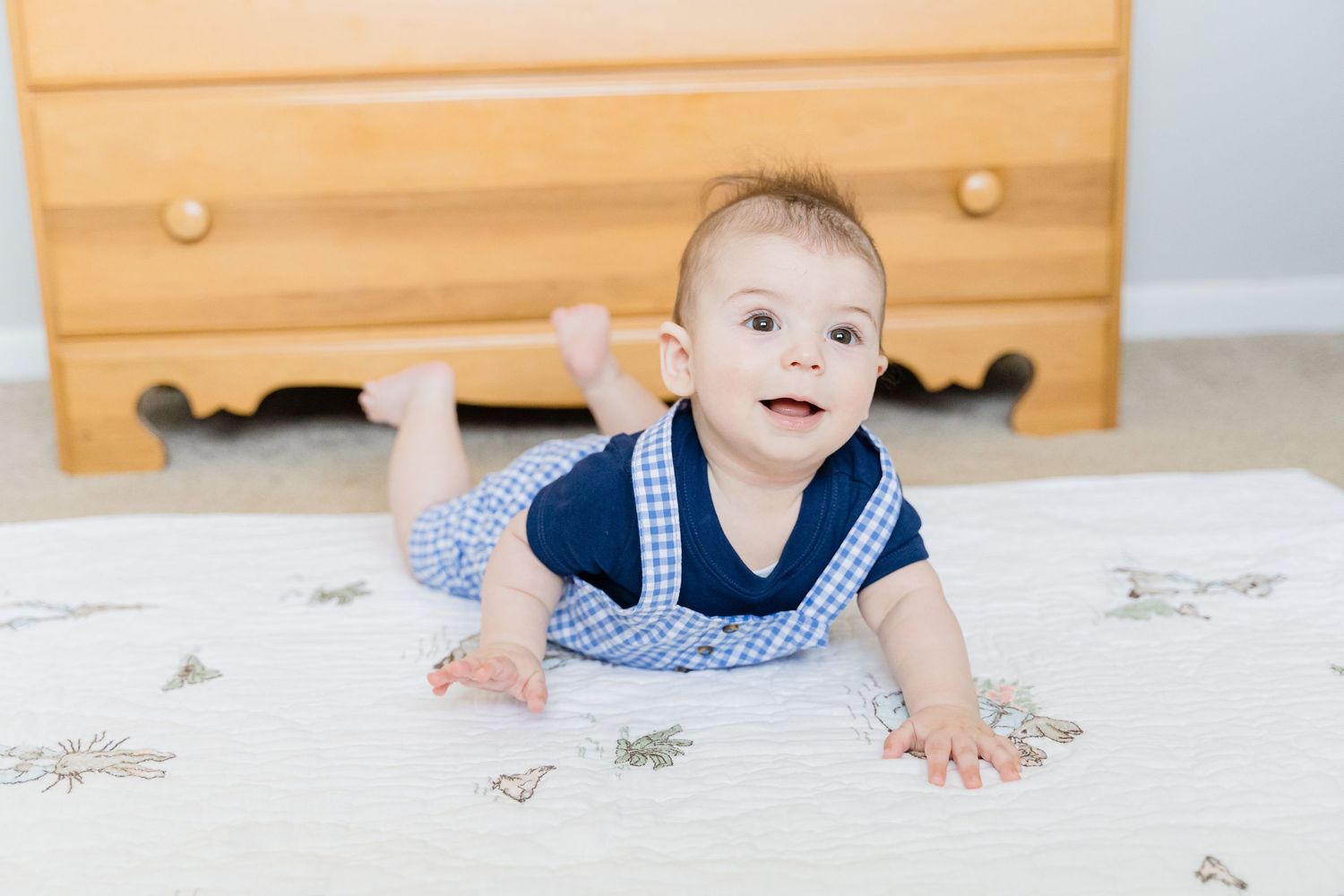 Baby in navy blue and white outfit crawls on white carpet while smiling and looking up.