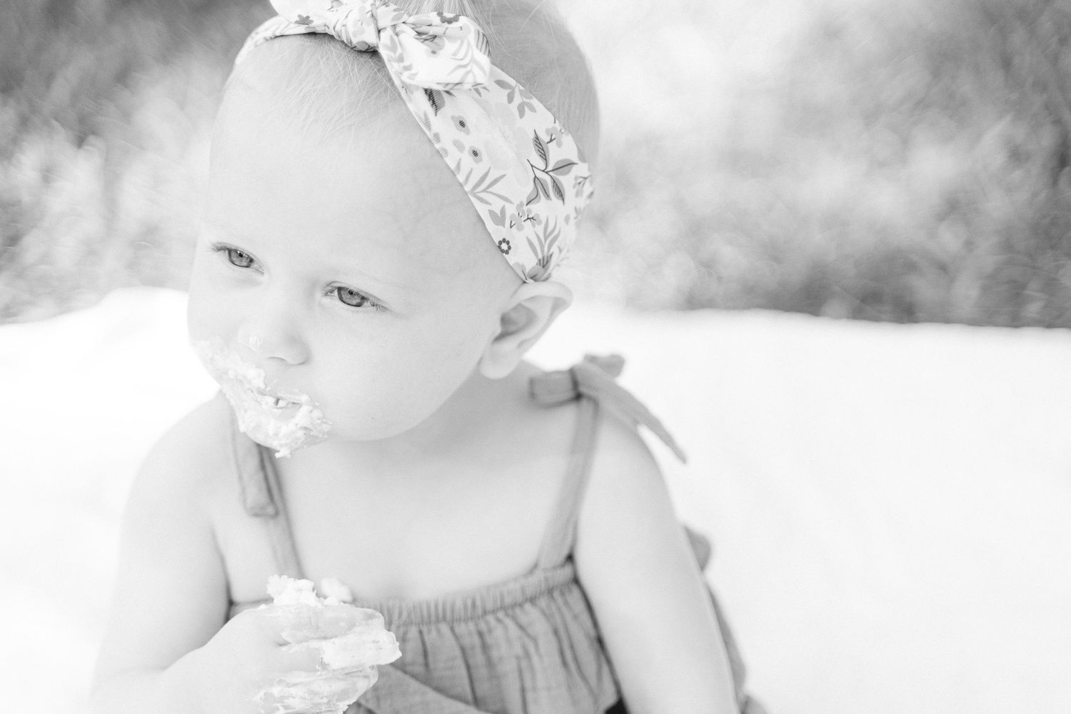 Black and white portrait of baby wearing floral headband on white blanket.
