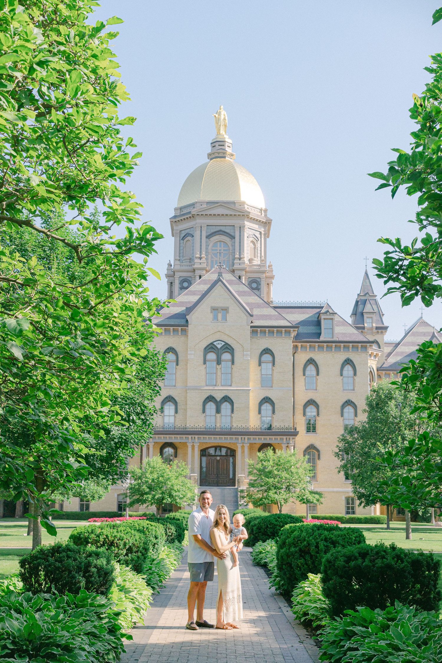 Golden domed Notre Dame campus building framed by green trees on a sunny summer day.