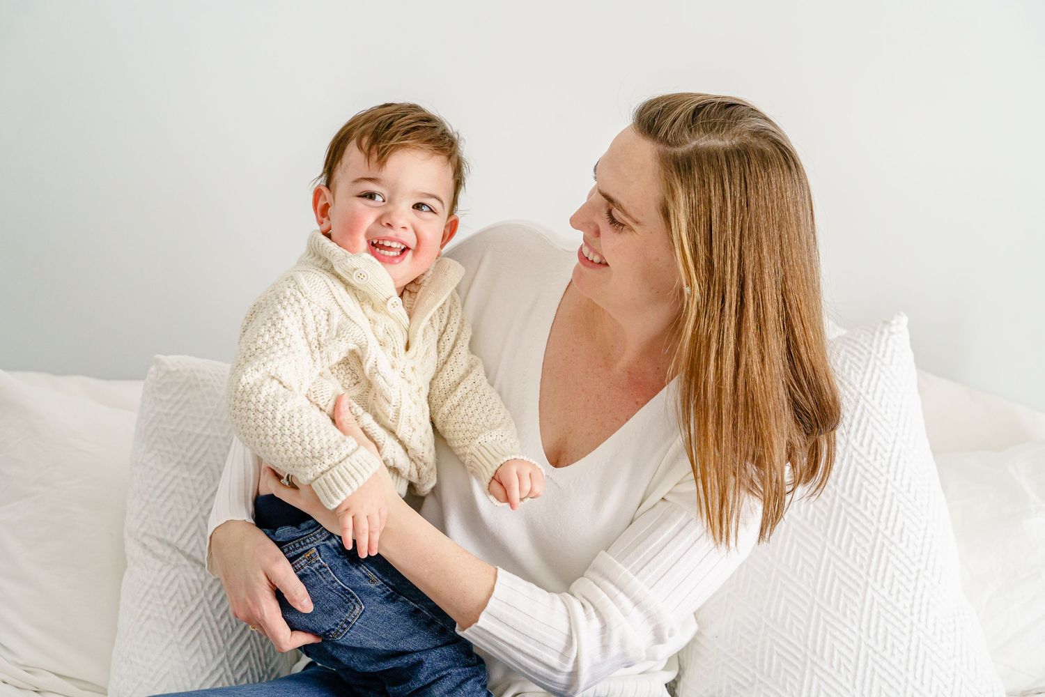 A joyful candid moment between parent and child sitting together on a white couch.
