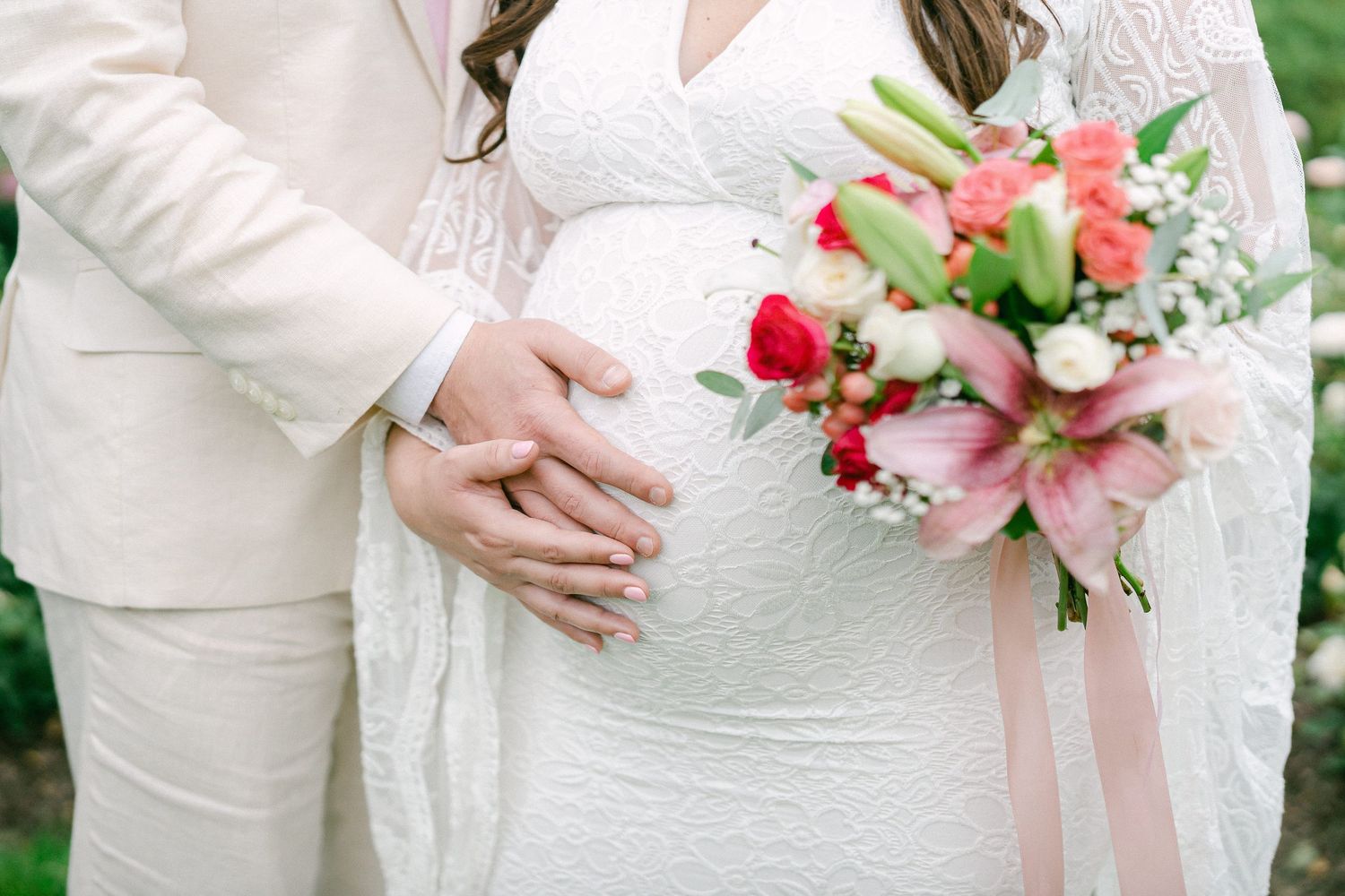 Wedding party members in blush pink dresses hold matching pink and white floral bouquets during an outdoor ceremony.