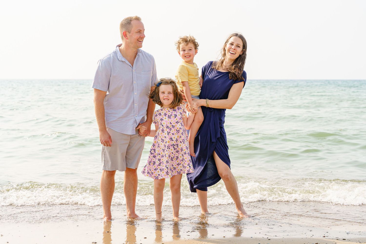 A group poses together on a bright sandy beach with turquoise ocean waters in the background.