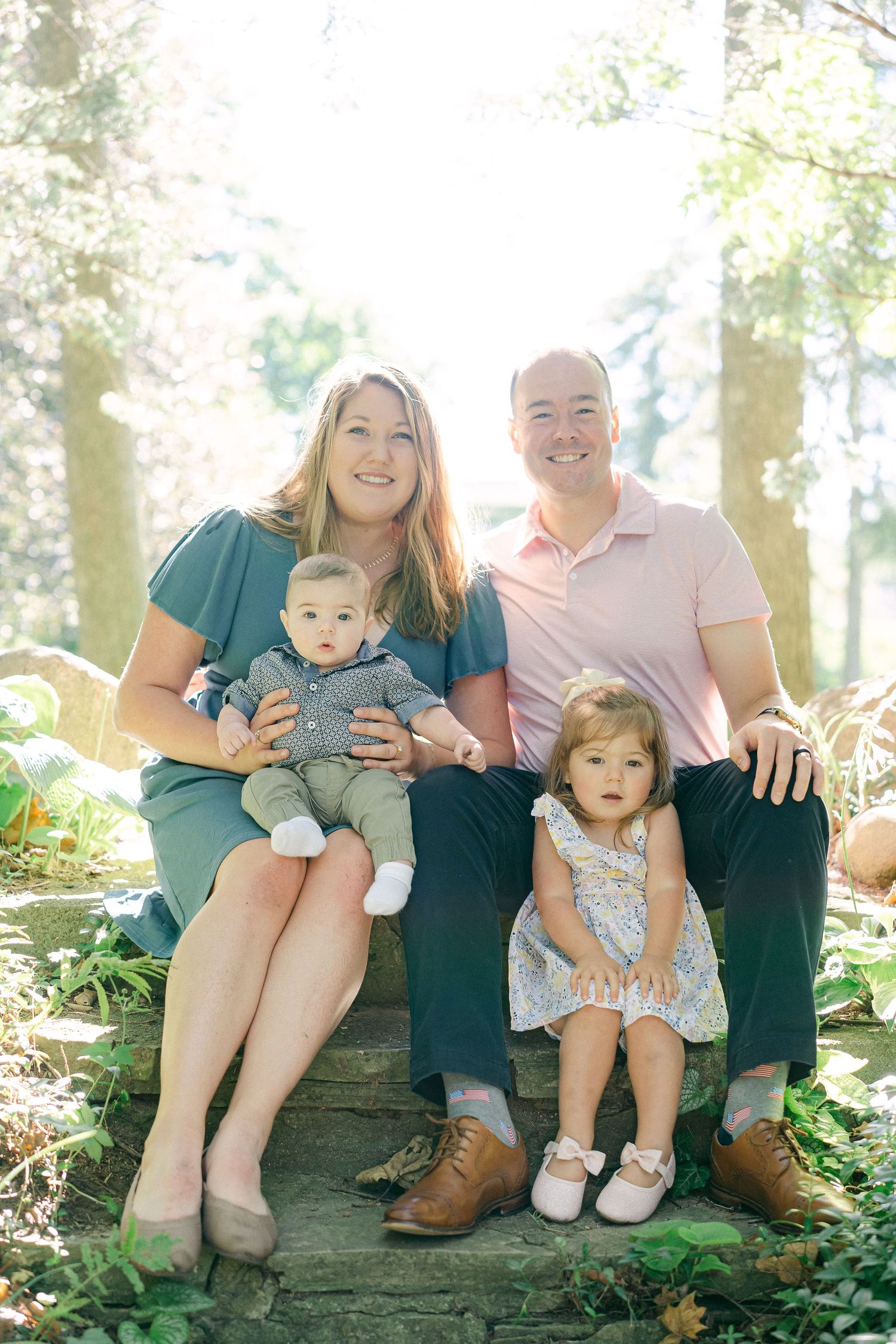 Family sitting together on rustic wooden steps in a sunlit forest setting.