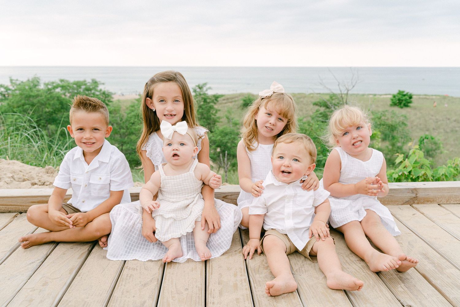 Children in white outfits sit together on wooden steps during an outdoor family photo session.