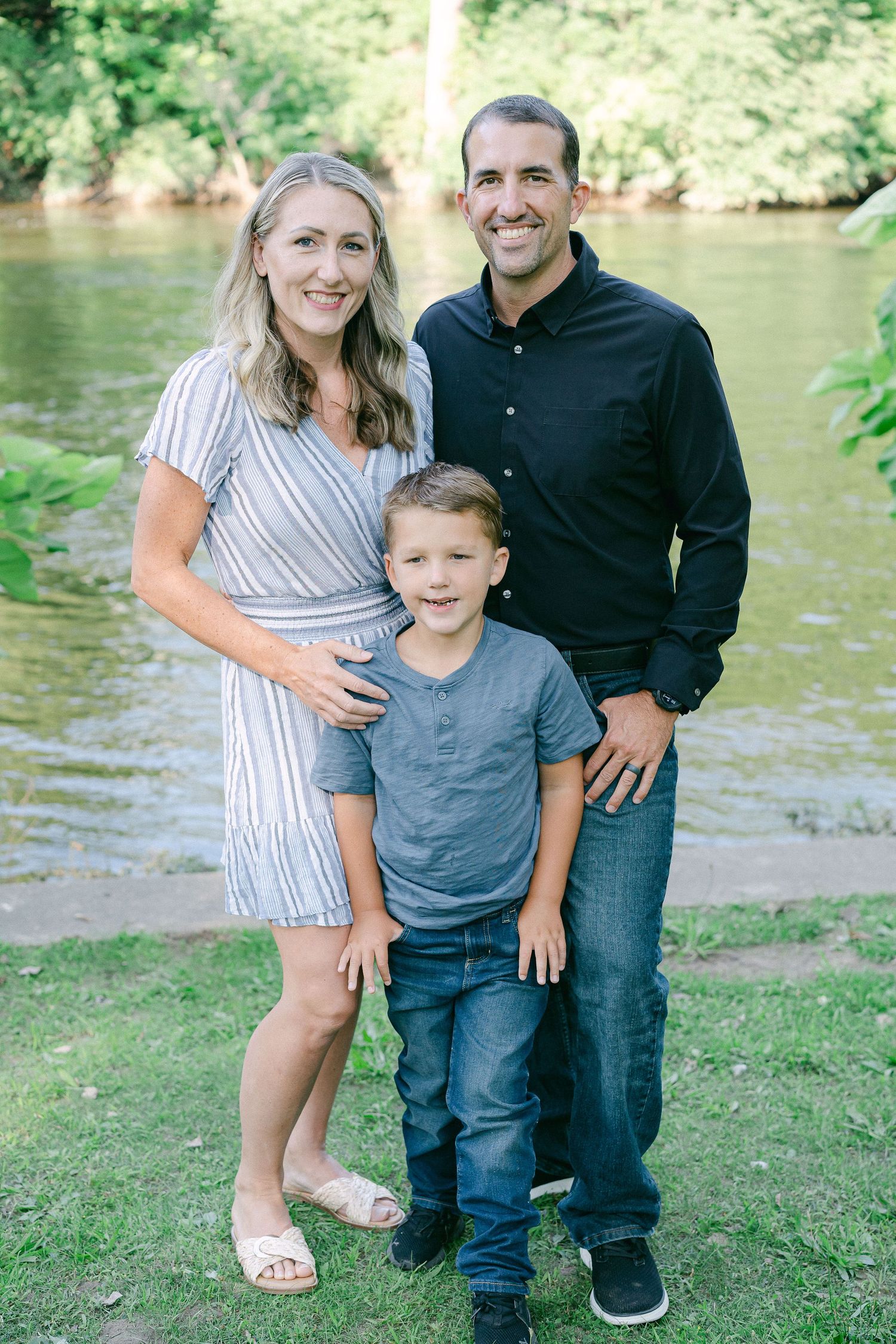 Family enjoying a summer day by the water's edge on grassy riverbank in matching casual outfits.