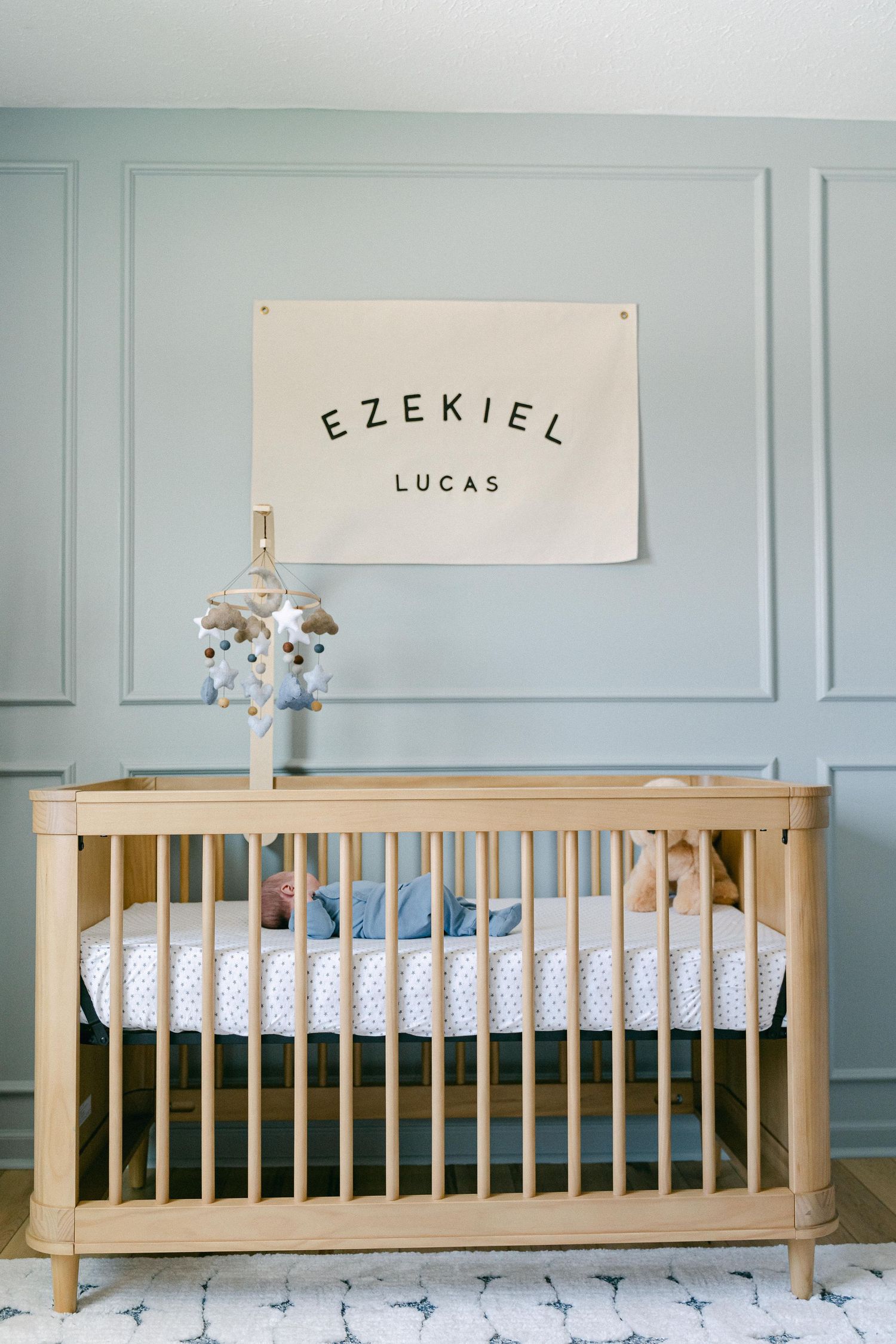 Wooden crib with white bedding and blue walls featuring decorative molding and a name sign above.