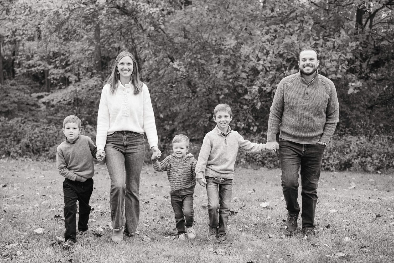 A sequence of black and white family portraits showing legs and feet walking together outdoors in nature.