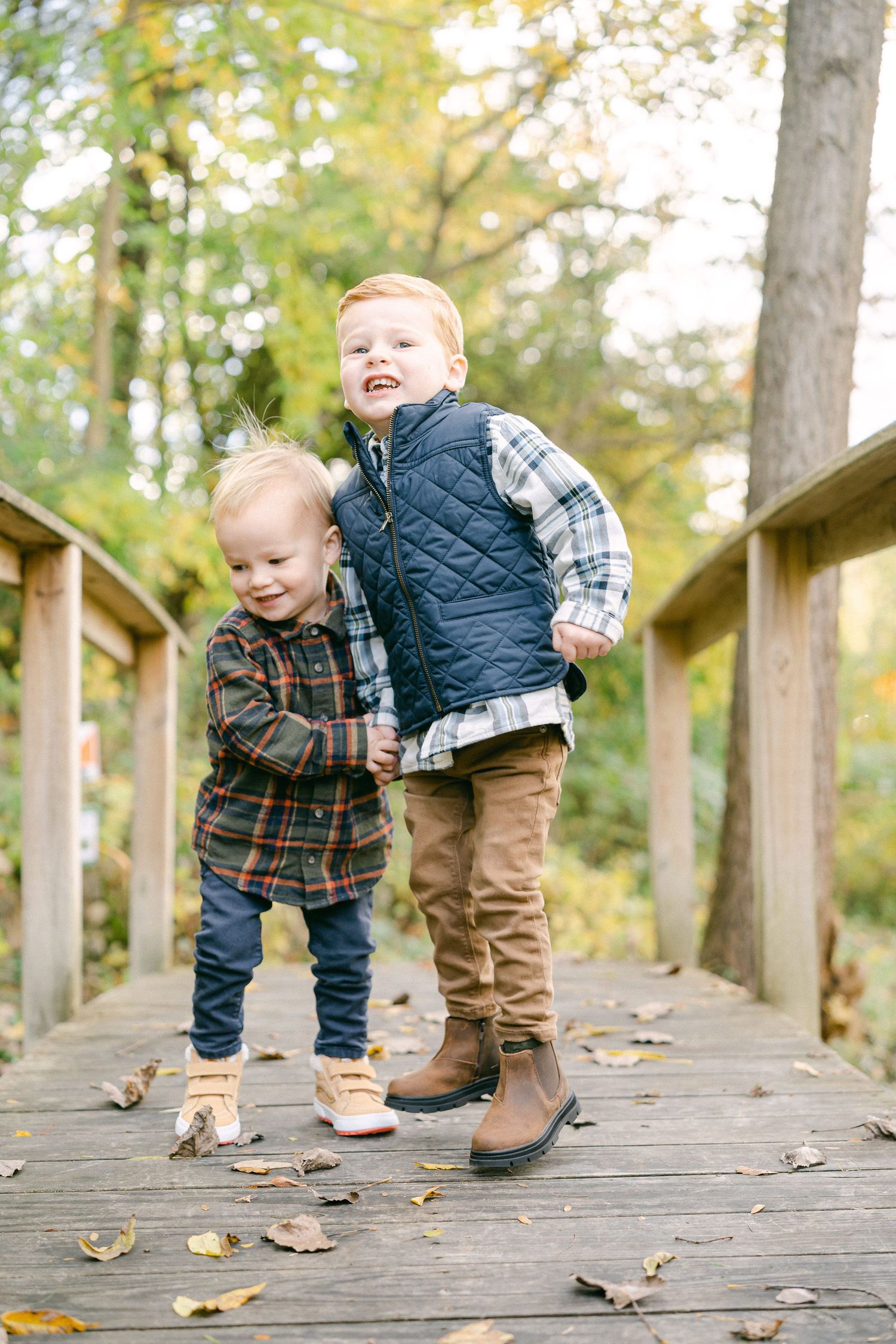 A series of playful photos showing a toddler walking and playing on a wooden boardwalk surrounded by autumn trees.