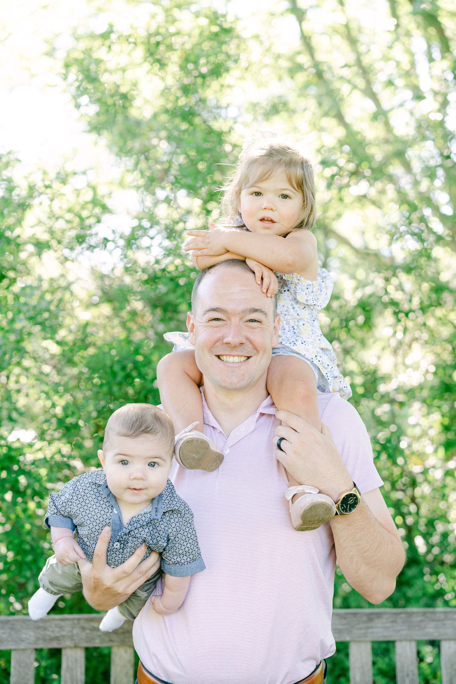 A family enjoying a playful moment together outdoors on a wooden bench surrounded by lush green foliage.