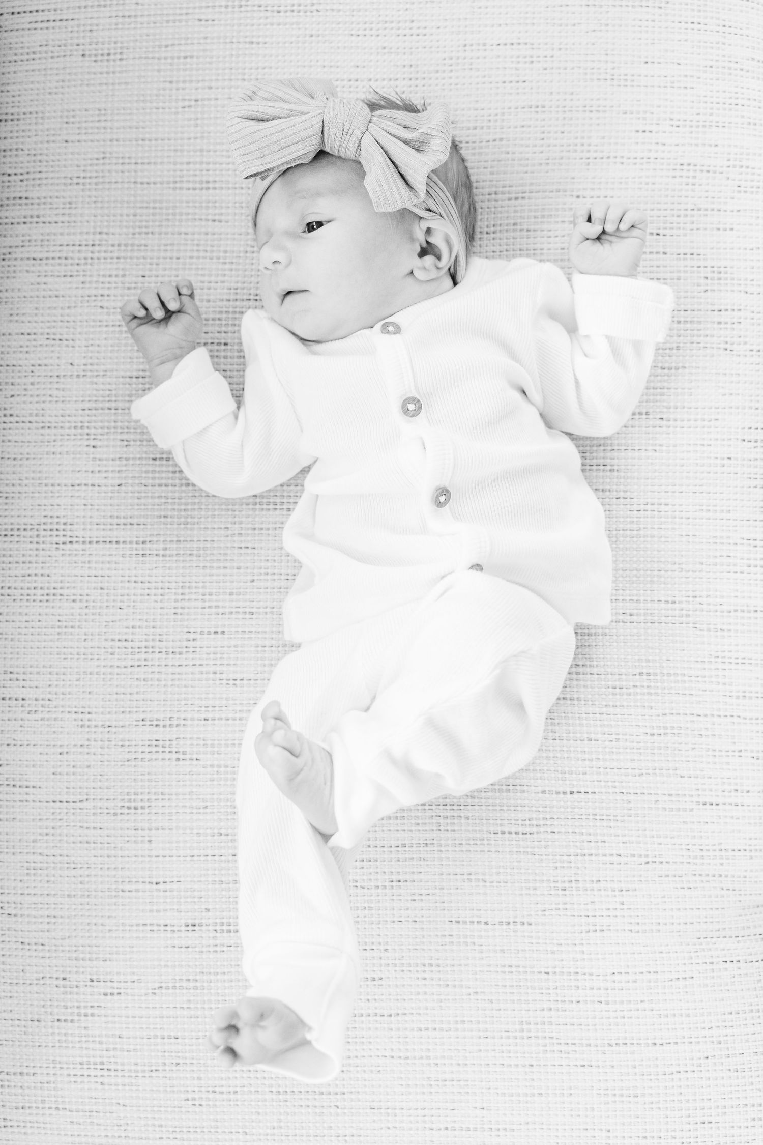 Peaceful newborn in white clothing resting on textured white fabric.