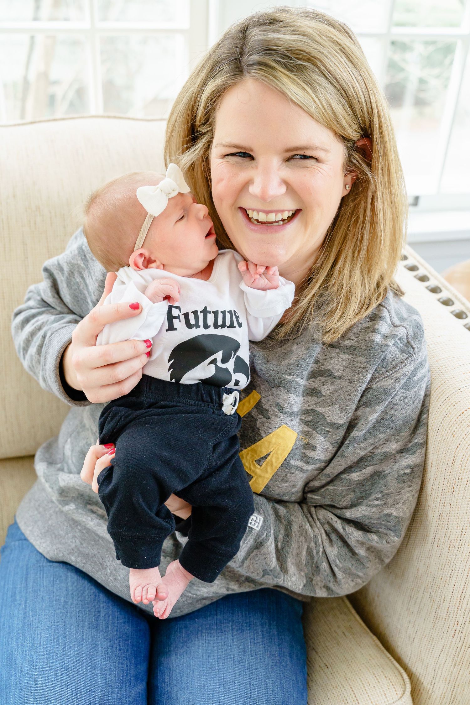 A parent holds a baby wearing a black onesie while sitting on a couch in a series of four photos.