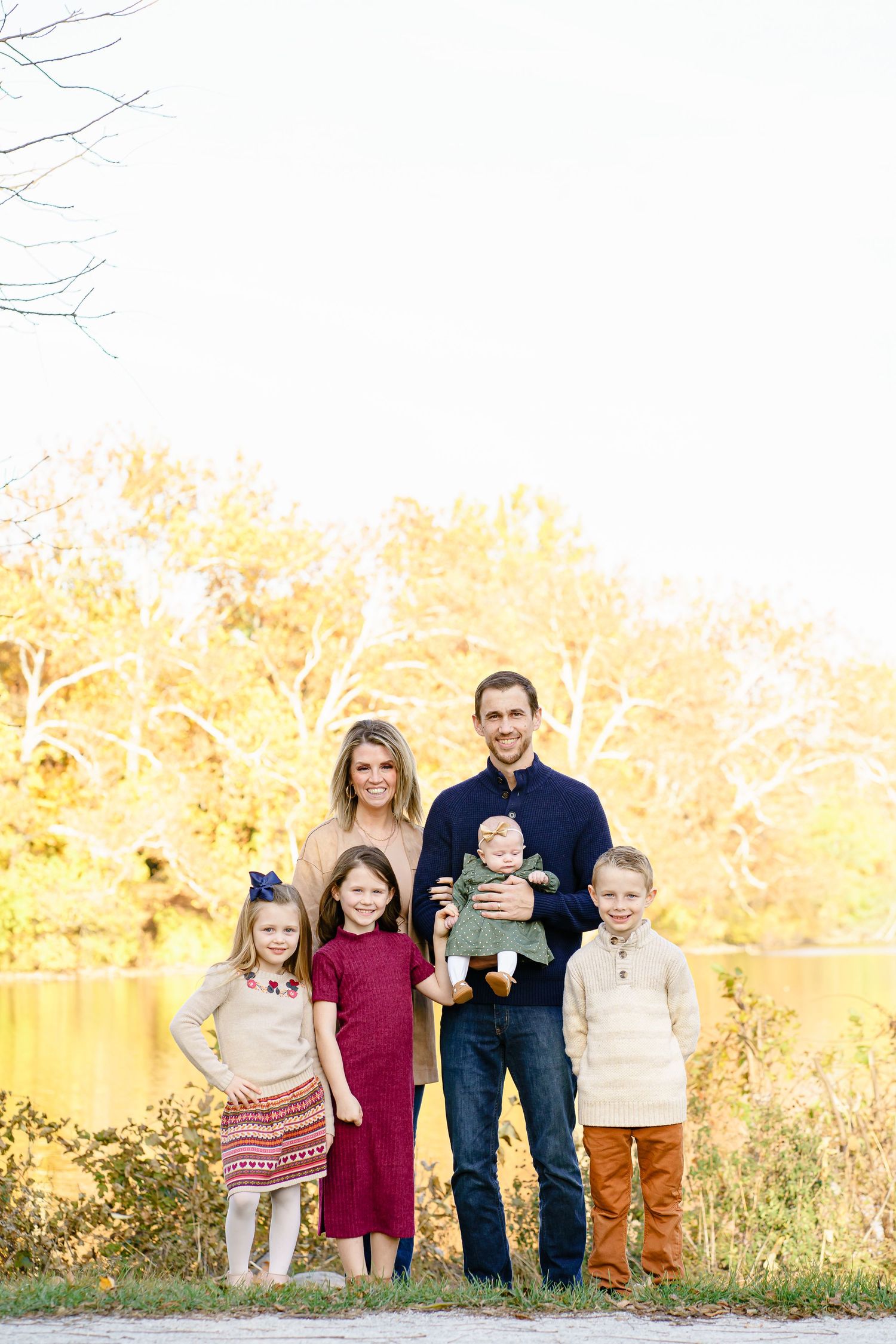 A family poses together outdoors during golden hour with autumn foliage in the background.