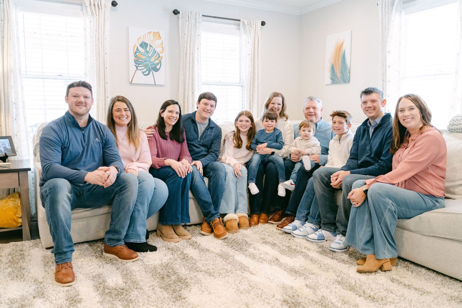 A group of people sitting together on gray couches in a bright living room with white walls and a plush area rug.