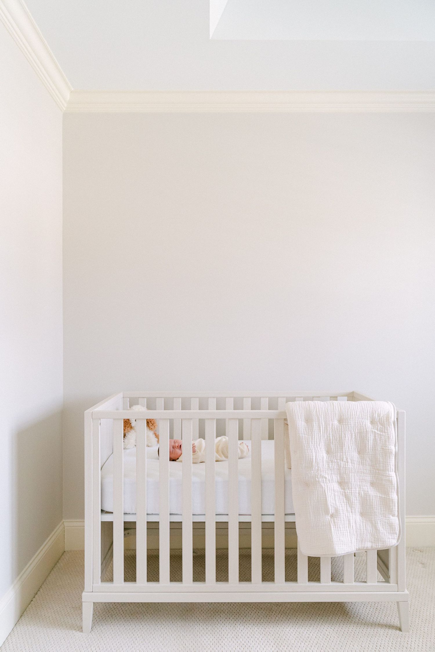 A minimalist white nursery with a classic wooden crib and soft blanket draped over the side.