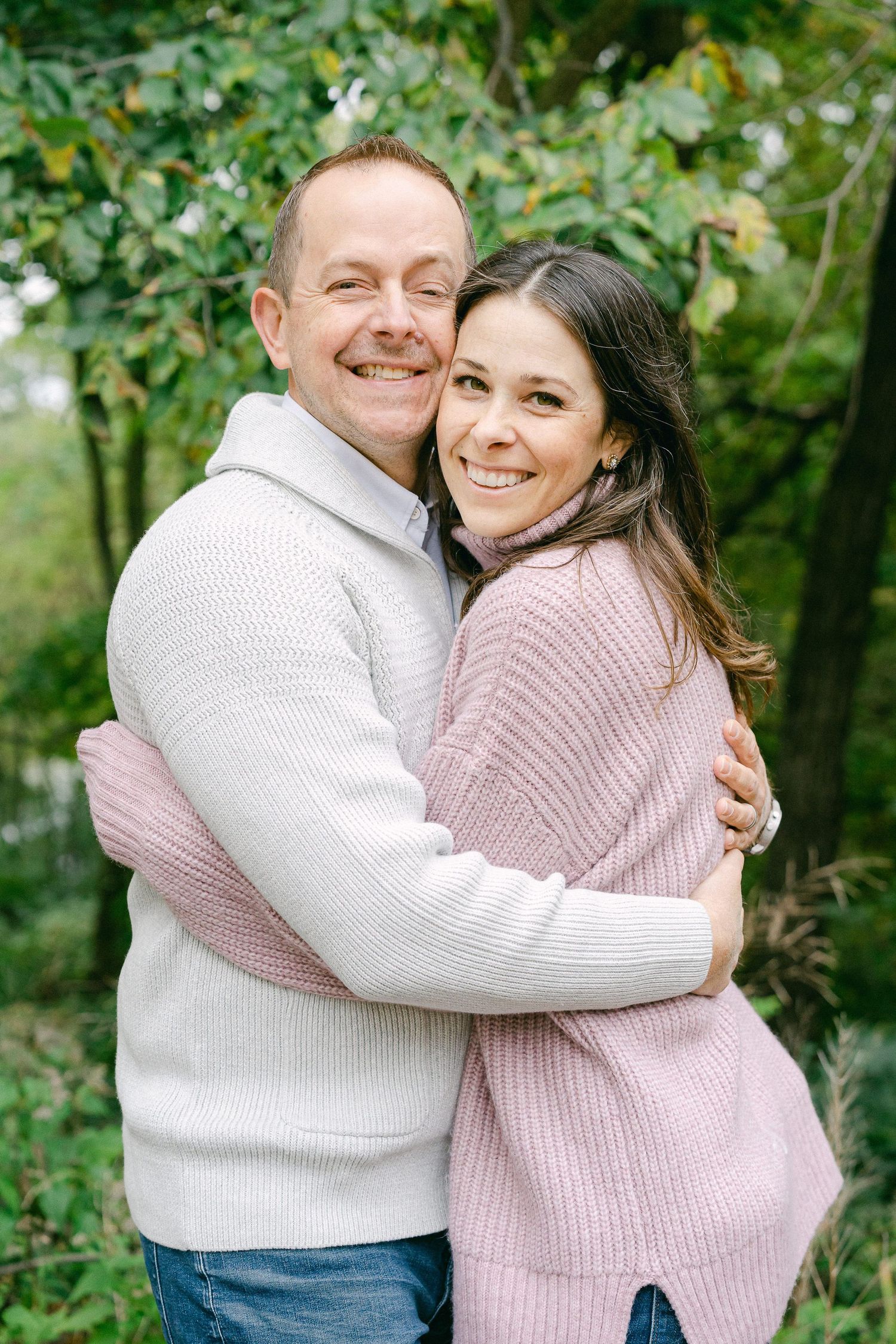Couple in matching knit sweaters share warm embraces while smiling outdoors in a natural setting.