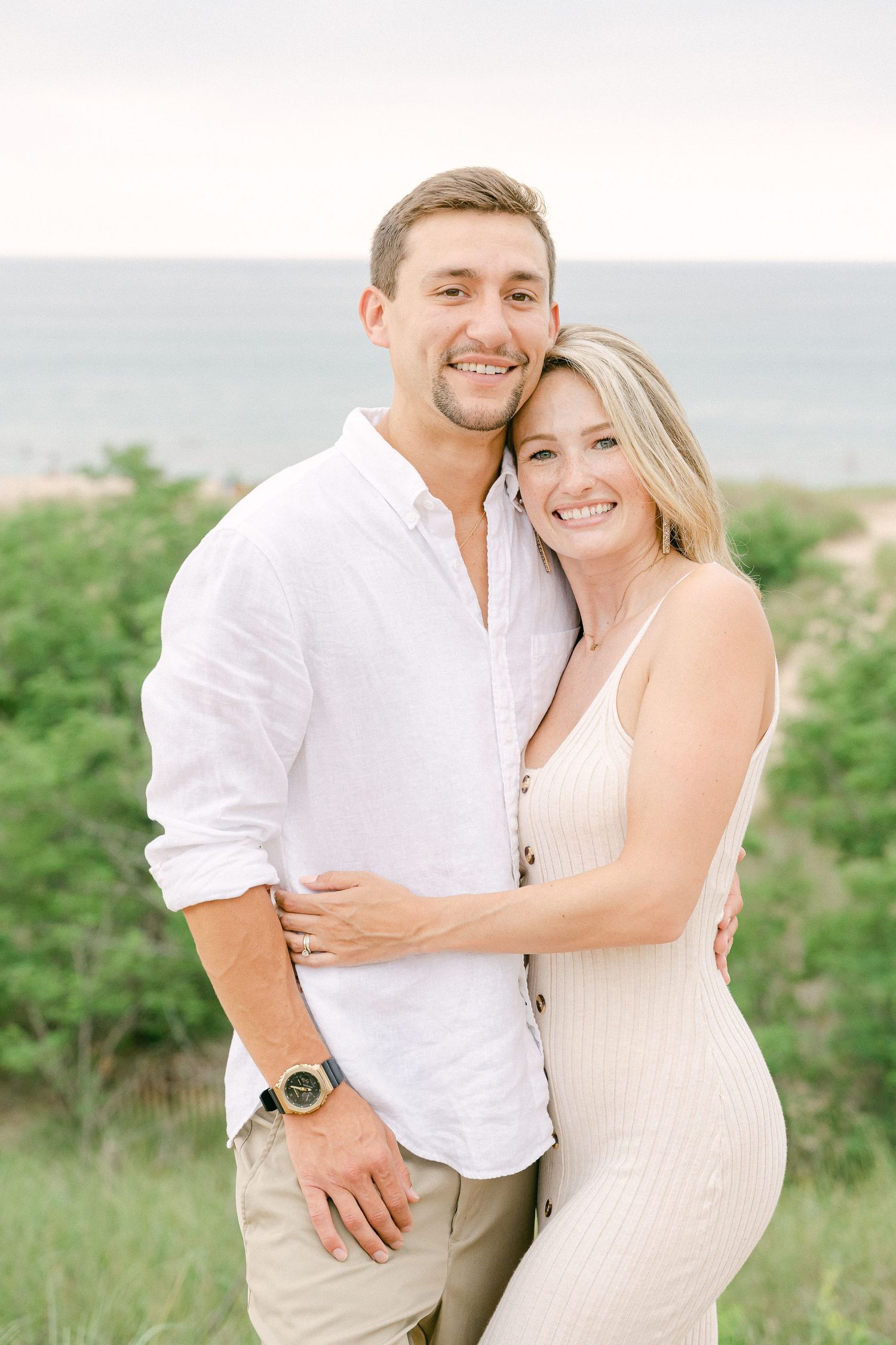 A couple embraces in a natural outdoor setting wearing coordinated white and cream outfits during a photo session.