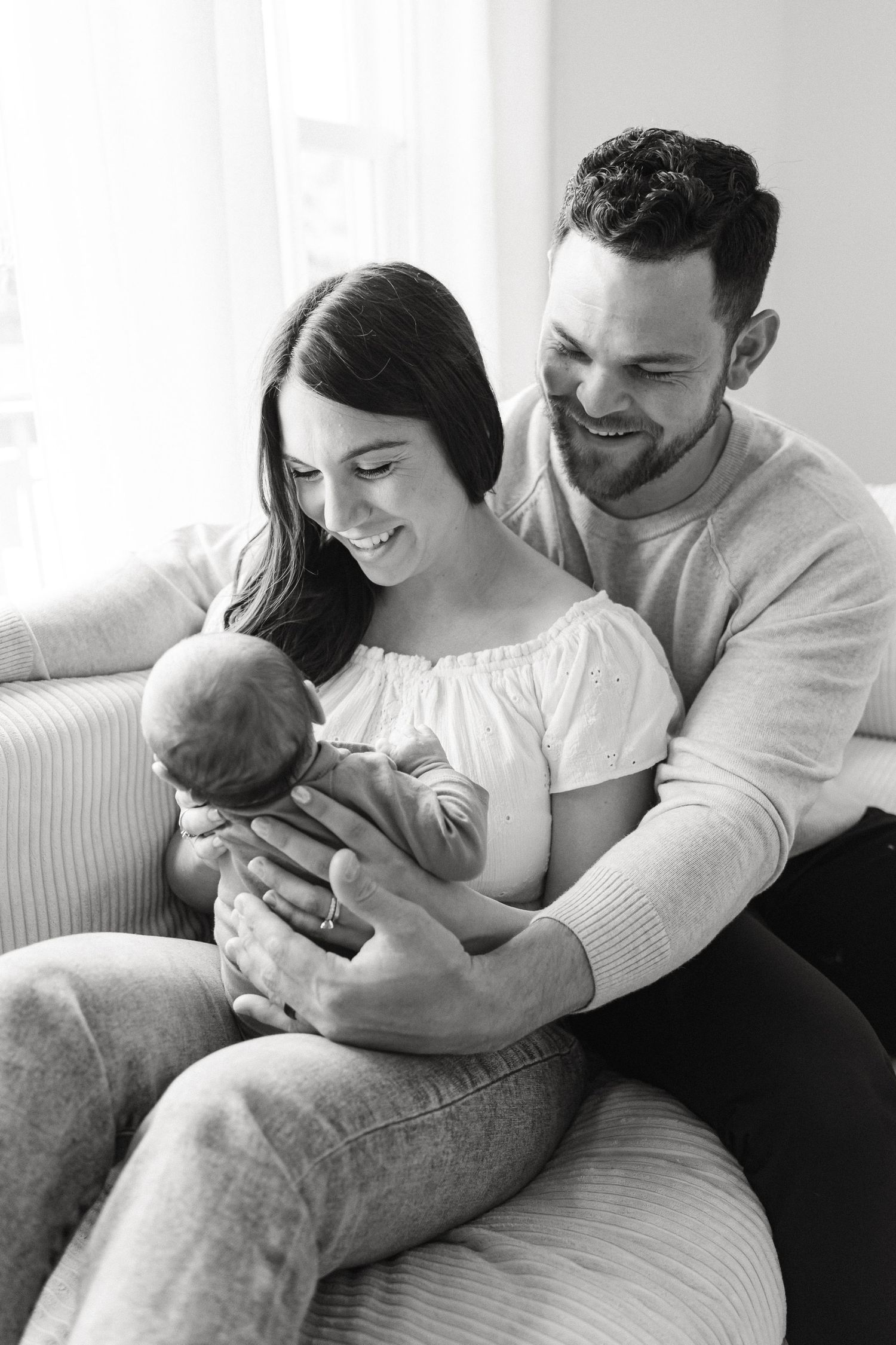A tender black and white portrait of new parents holding their newborn baby on a couch.