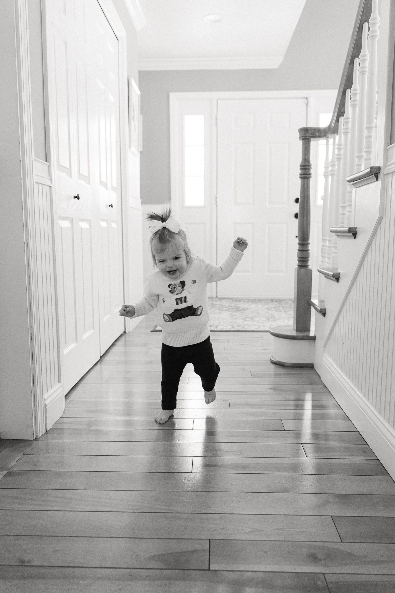 A sequence of black and white photos showing a toddler crawling and playing in a bright hallway with wooden floors.