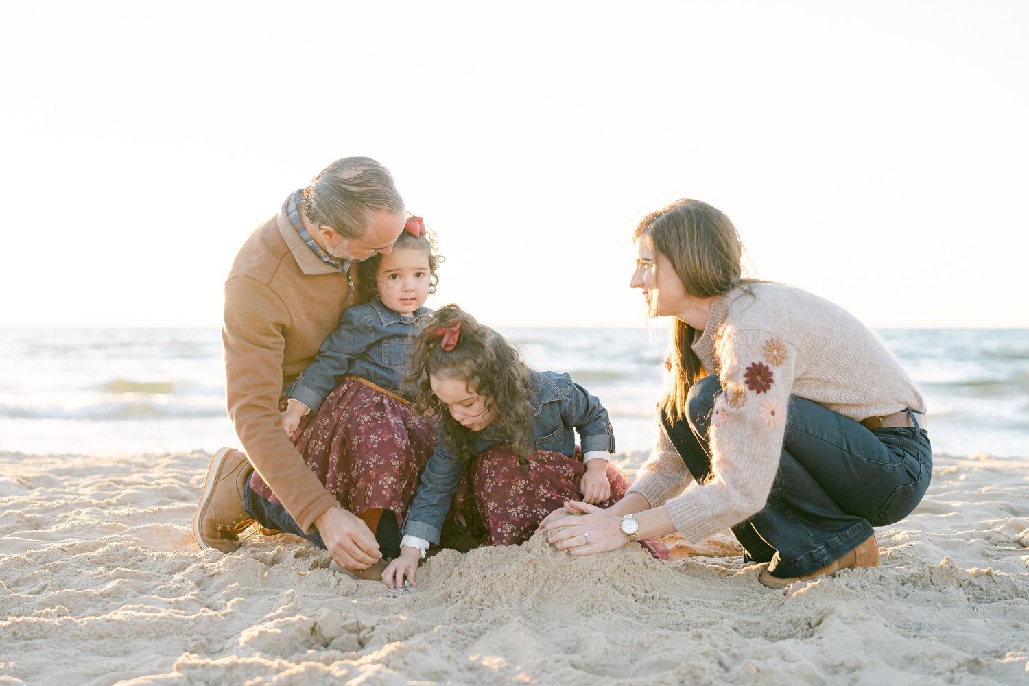 Family with dog enjoying playful moments together on a sunny beach at sunset.