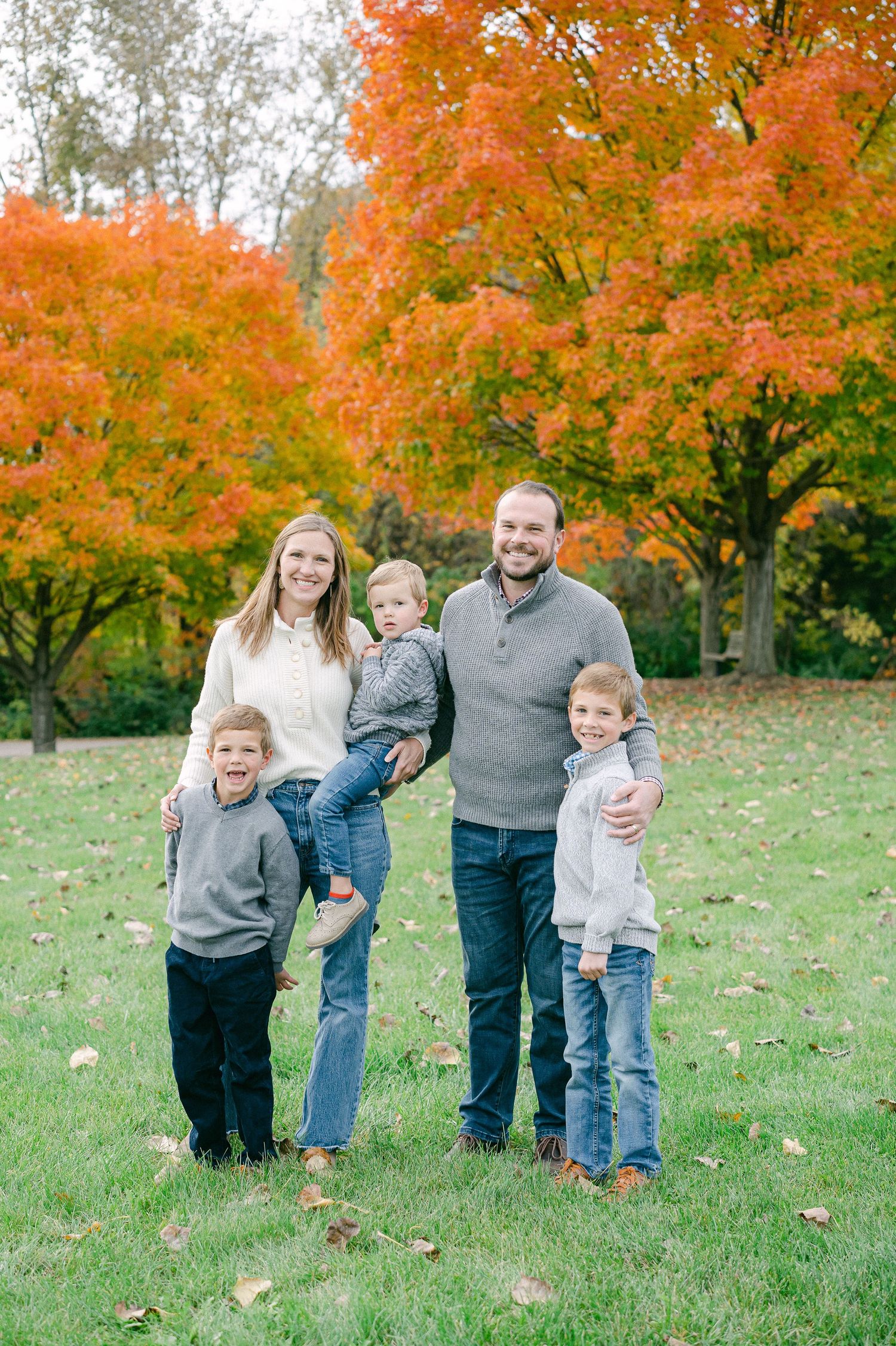 A group stands together on a grassy hill with vibrant orange autumn trees creating a stunning fall backdrop.