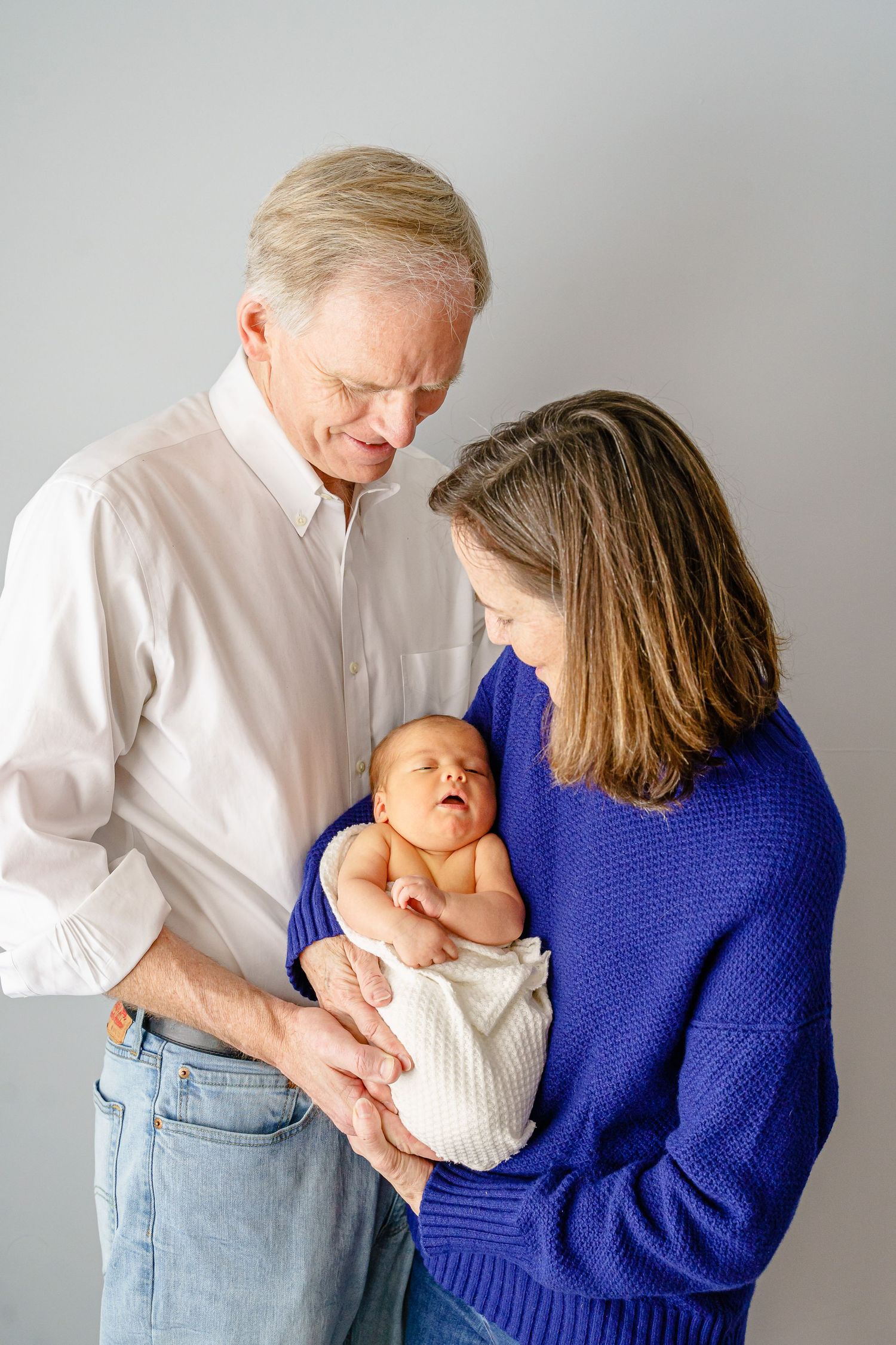 A series of tender moments between a parent and baby in white and blue clothing against a light background.