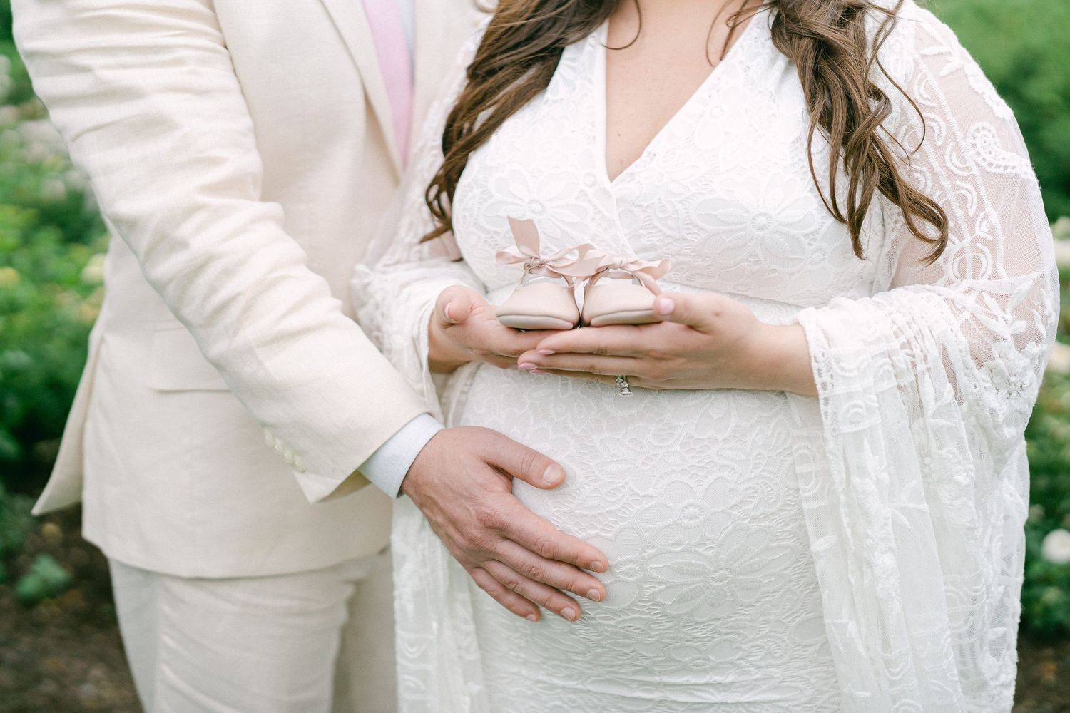 A series of photos showing a pregnant person in a white lace dress cradling their baby bump in a garden setting.