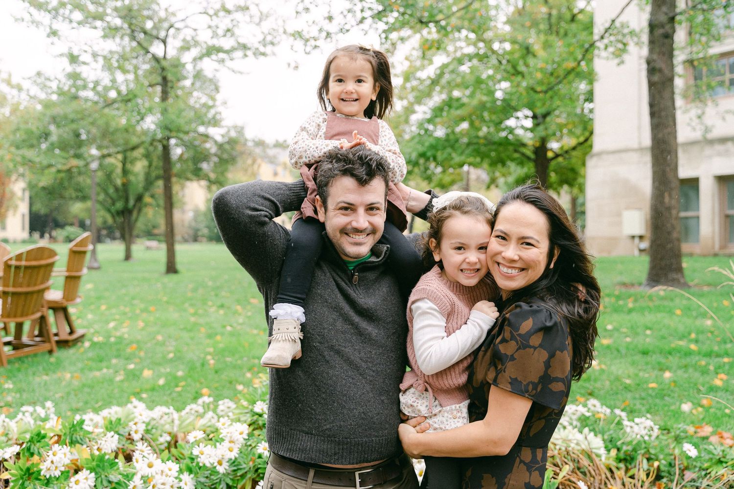 A happy family laughs and embraces while taking outdoor portraits in a grassy park setting.
