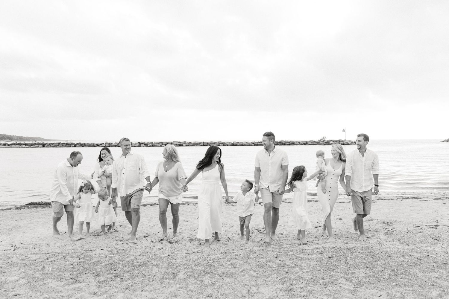 A group poses along a sandy beach in a black and white panoramic shot creating a joyful silhouette.
