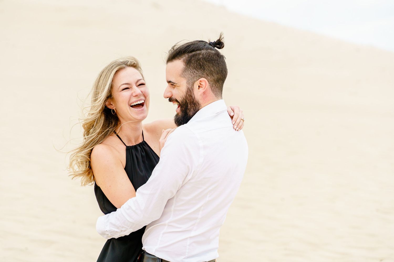 A couple embraces and laughs together during a romantic photoshoot on a light beige background.