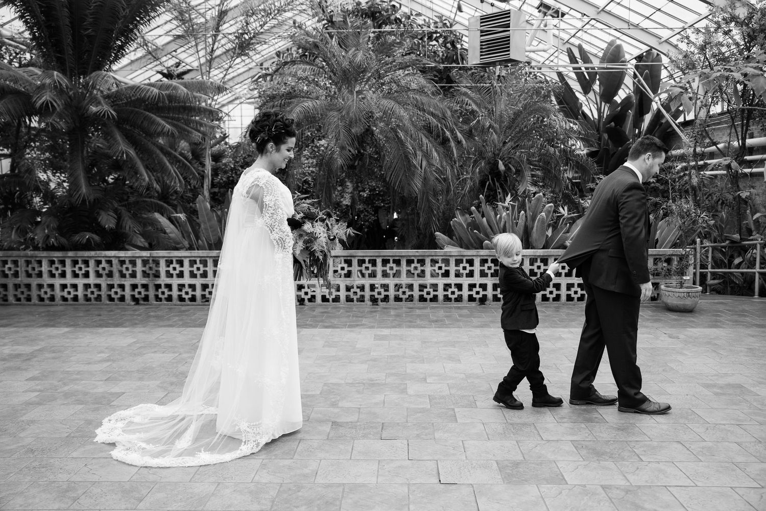 Black and white wedding photo of bride in white gown with child and groom in botanical garden greenhouse in South Bend, IN
