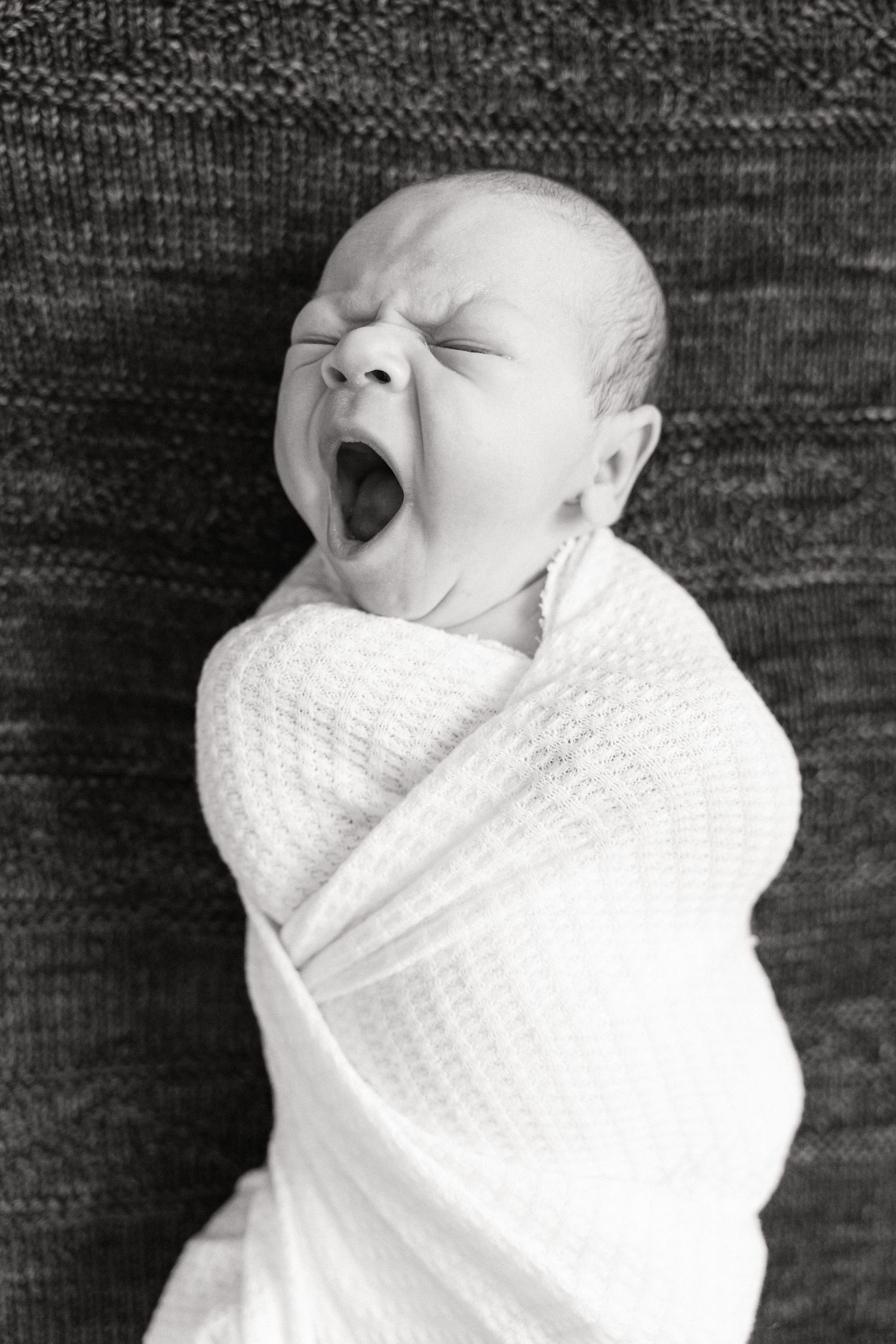 Black and white photo of a newborn swaddled in white fabric against a dark background.