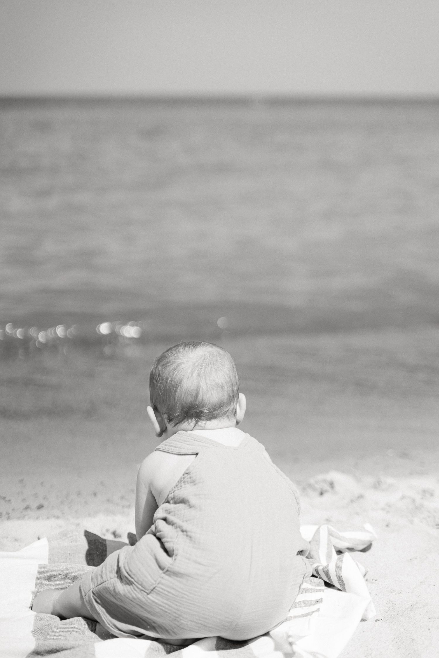 A sequence of black and white images showing a baby crawling on a sandy beach near the ocean waves.