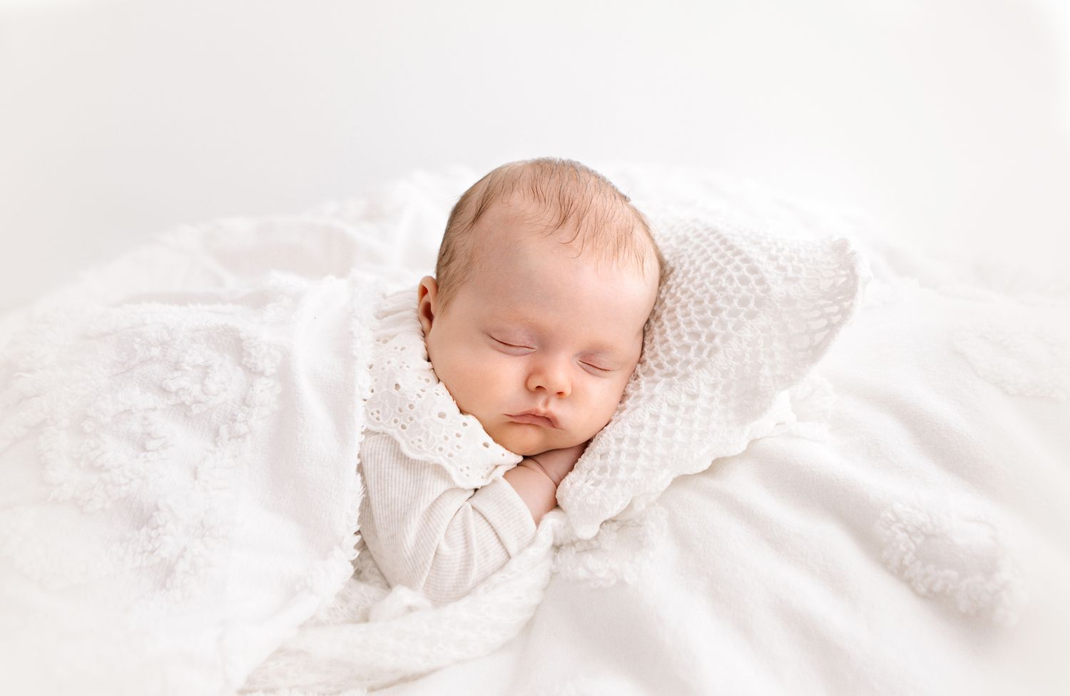 Peaceful newborn baby sleeping wrapped in a soft white knit blanket on a white background.