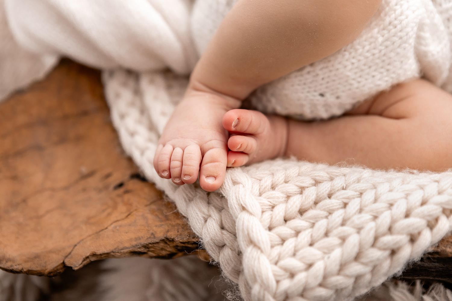 Close-up of tiny newborn baby feet resting on a chunky white knit blanket over rustic wood.