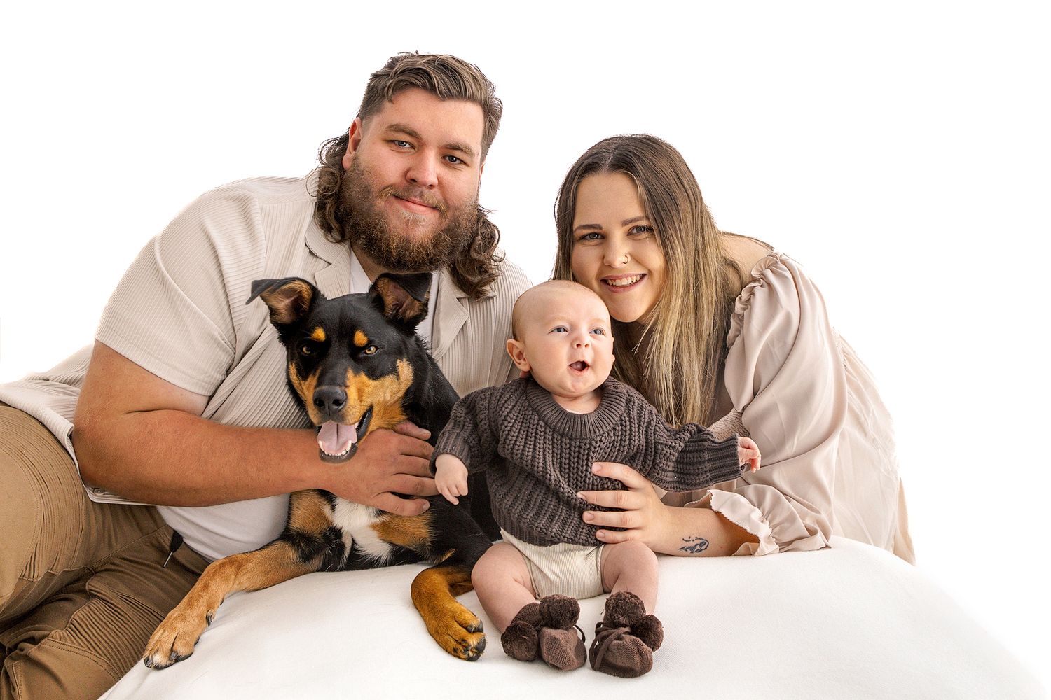 Happy family with bearded dad, smiling mom, baby, and dog posing together.