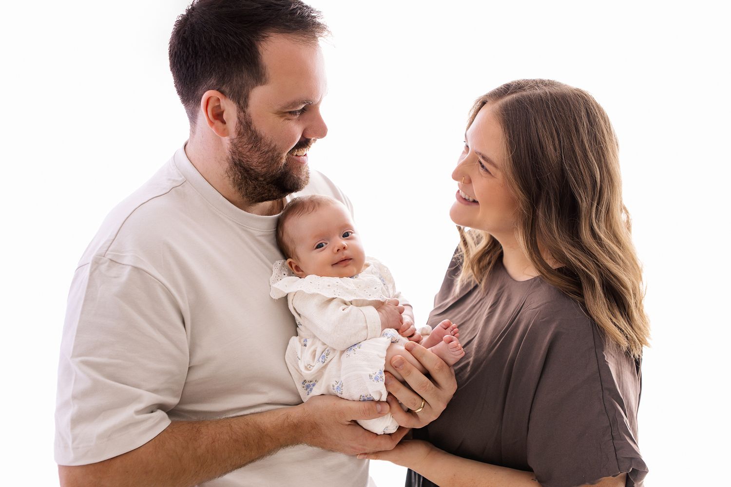 Happy parents holding their newborn baby during a professional white background family portrait session.