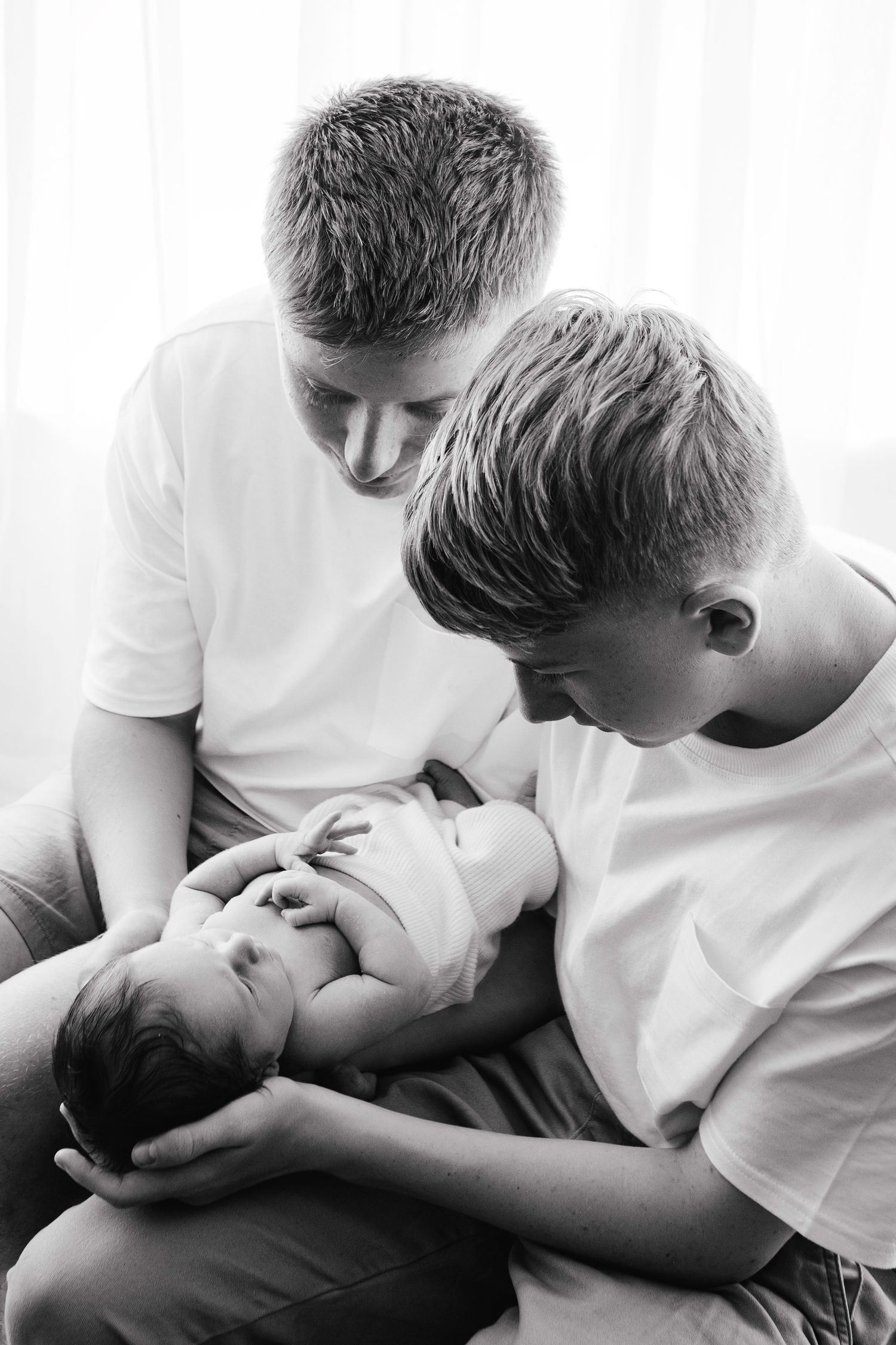Black and white photo of two boys in white shirts tenderly holding newborn baby.